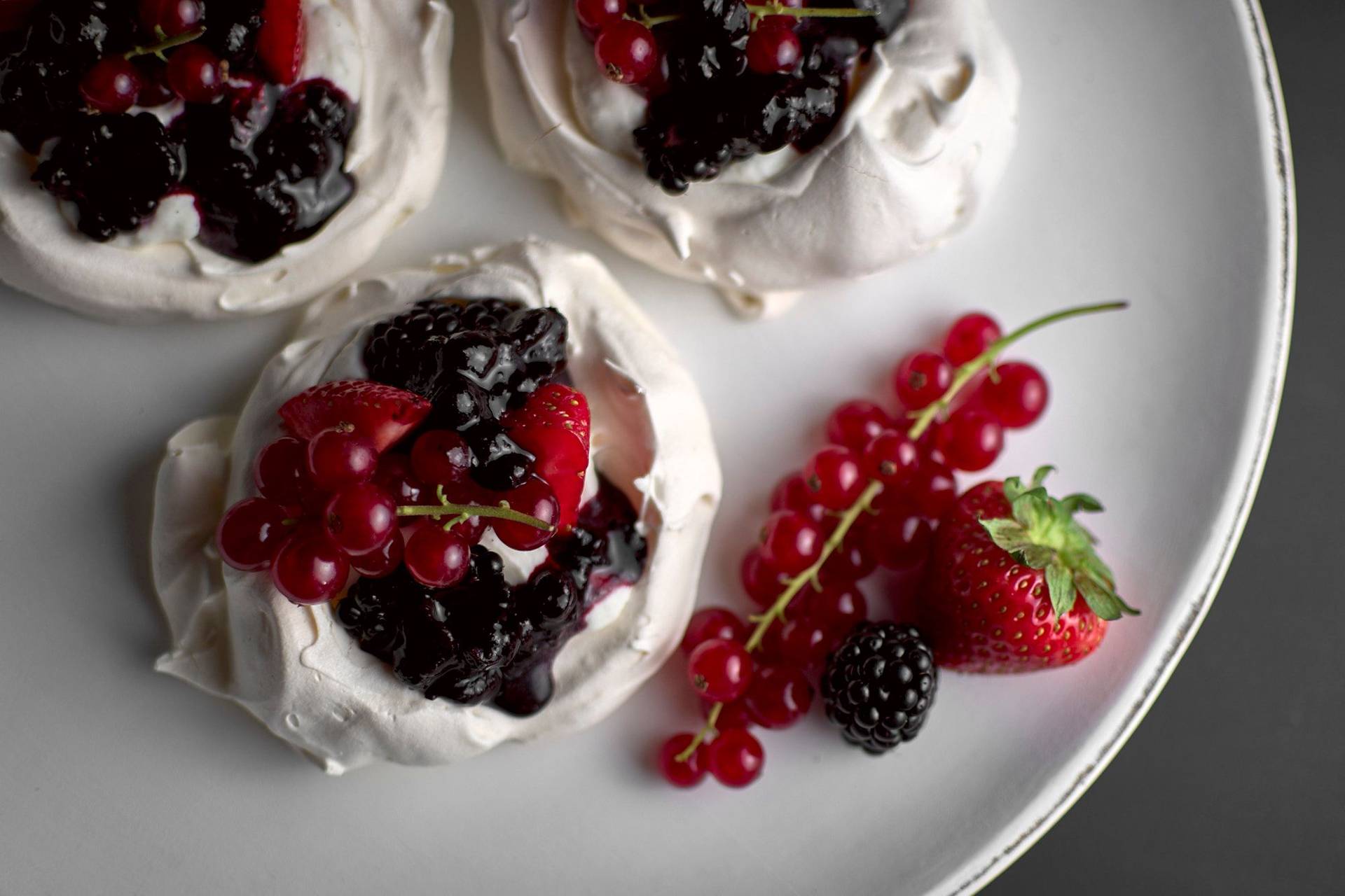 pavlova with berries and salted cream on a white plate with black background