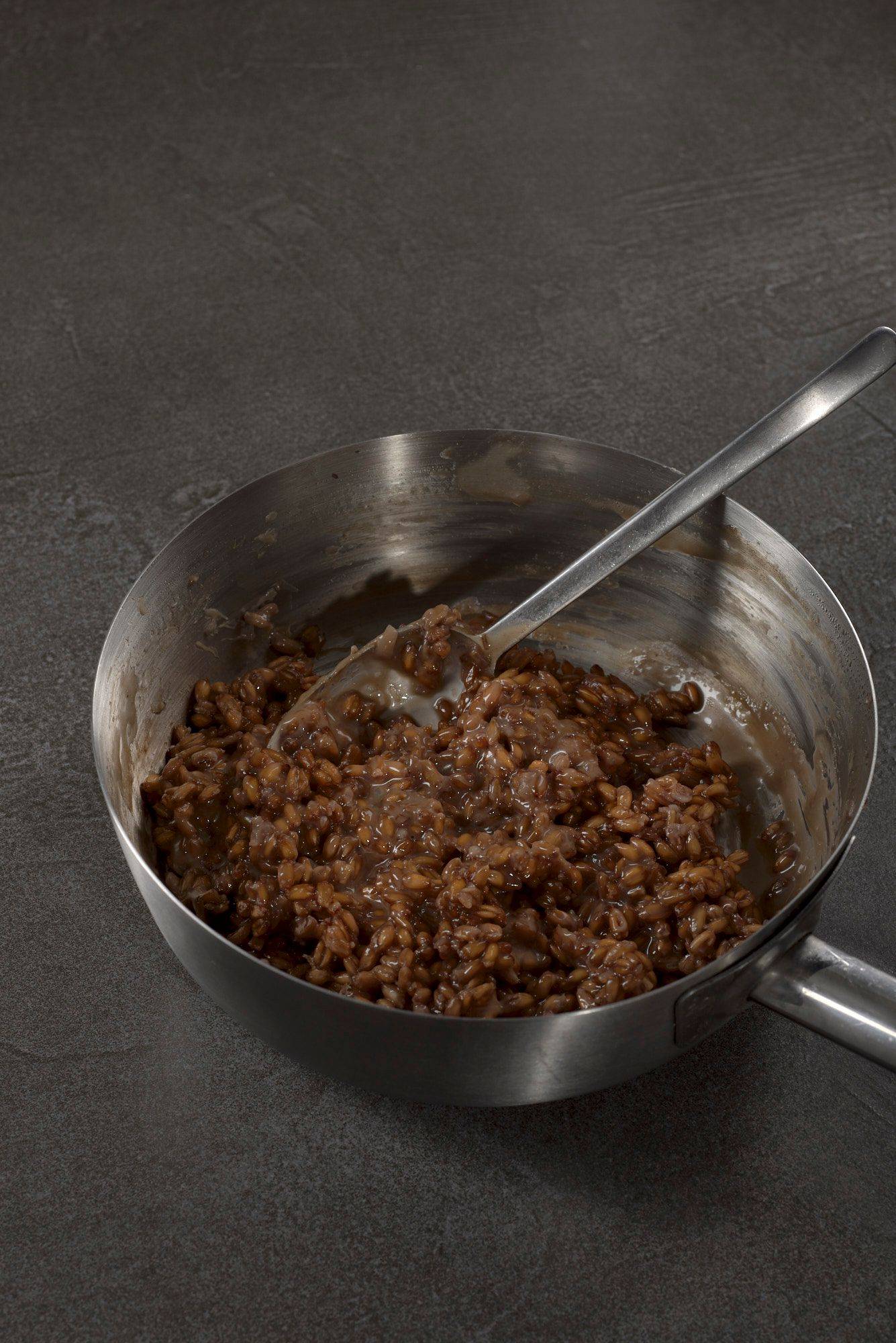 spelt risotto with harzer cheese in a metal sauce pan on a gray sapienstone top with green background