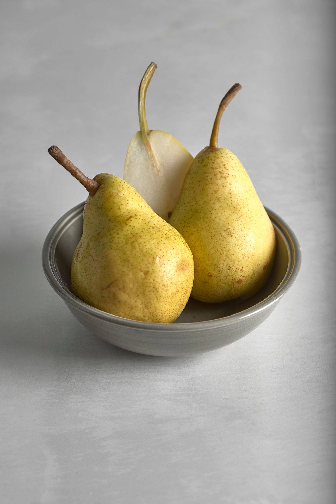 three pears in a gray ceramic bowl on a white stone table