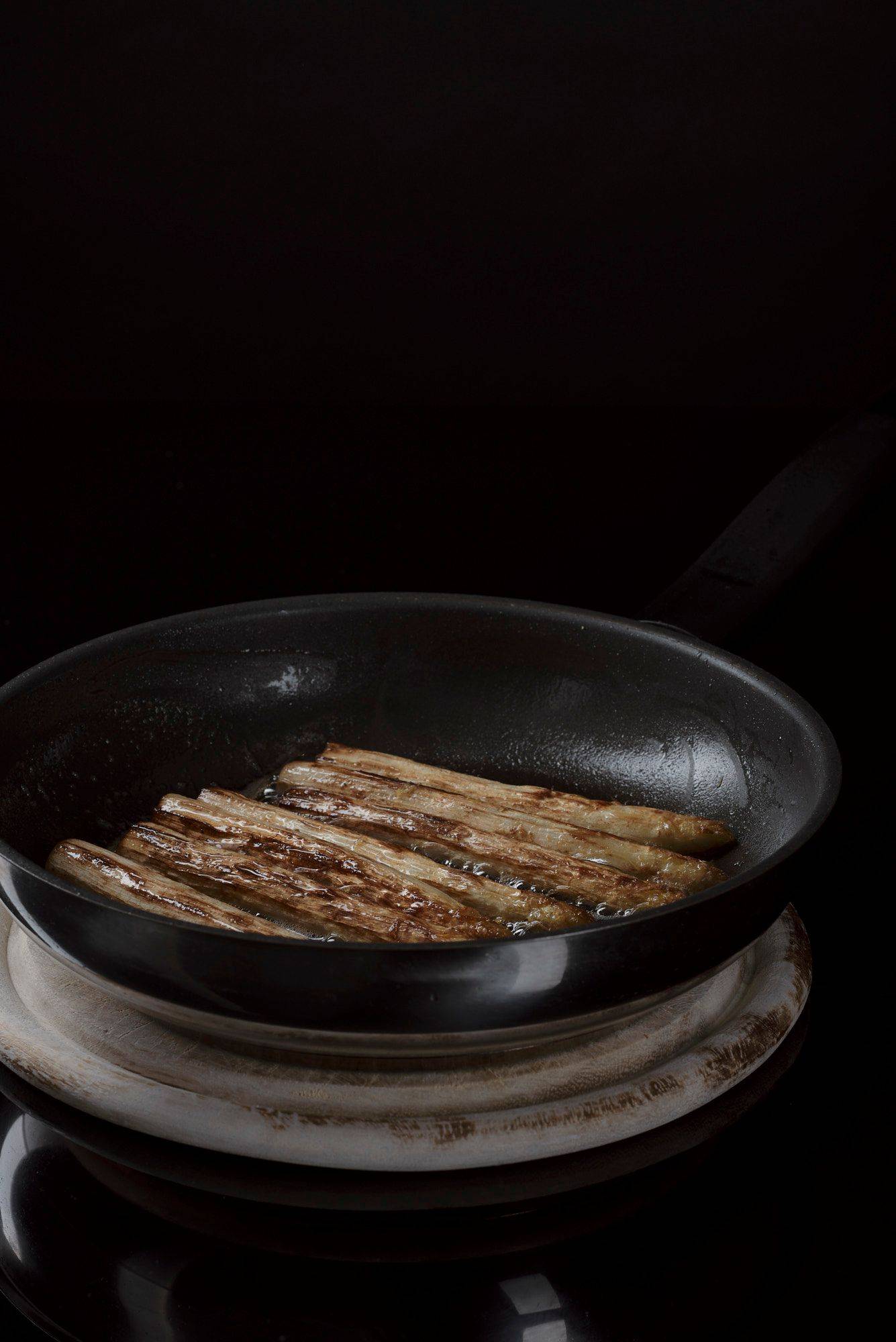 roasted asparagus in a frying pan with black background