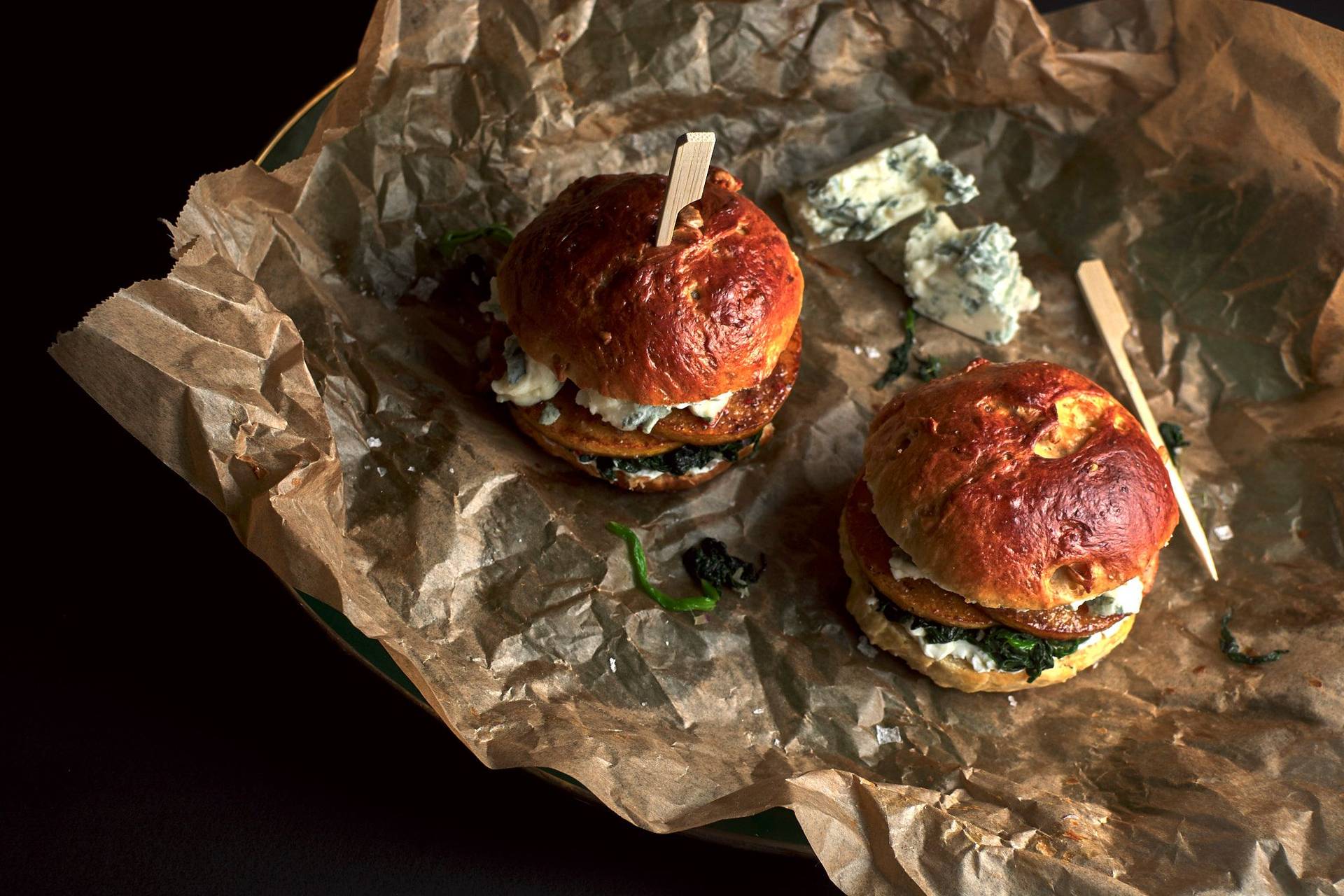 vegetarischer Kürbis-Brioche Burger mit Blauschimmel Käse und Spinat vor schwarzem Hintergrund