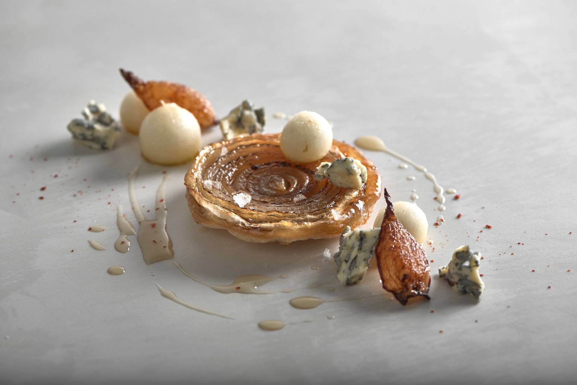 onion tarte tatin with blue cheese and pear on a white stone table