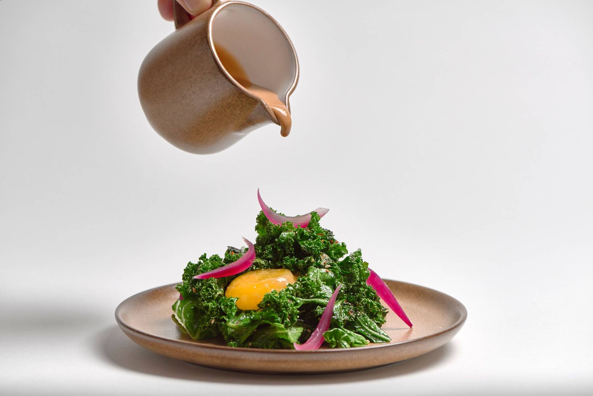 grünkohl salat mit miso eigelb und hagebutte auf einem braunen keramik teller mit weißem hintergrund