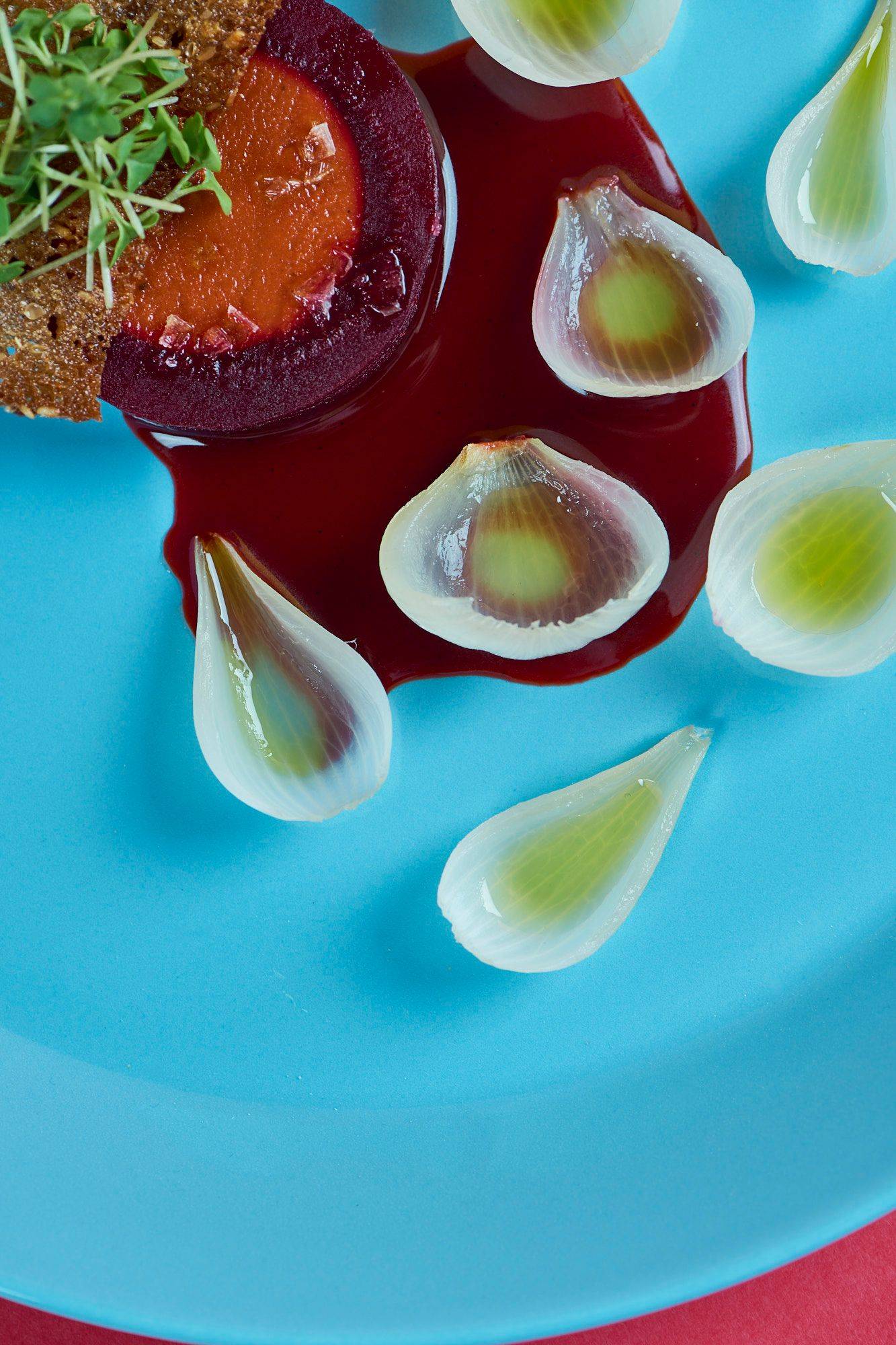 gebackene rote beete mit zwiebeln und veganer jus mit chilenischem wein von cono sur auf einem blauen teller mit rotem hintergrund