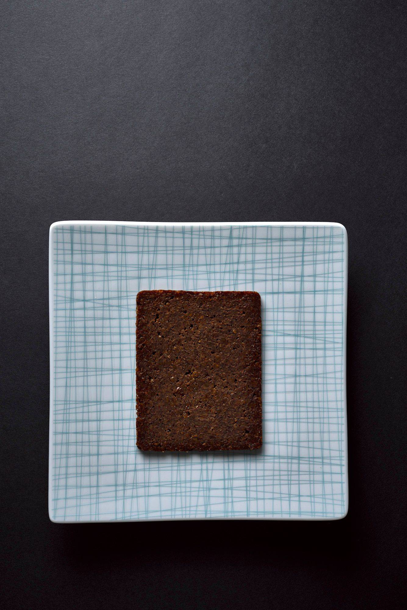 eine scheibe pumpernickel auf einem tellerbasilikum und orange gebeizter saibling mit rhabarber und tee mayonnaise auf einem blauen teller mit schwarzem hintergrund