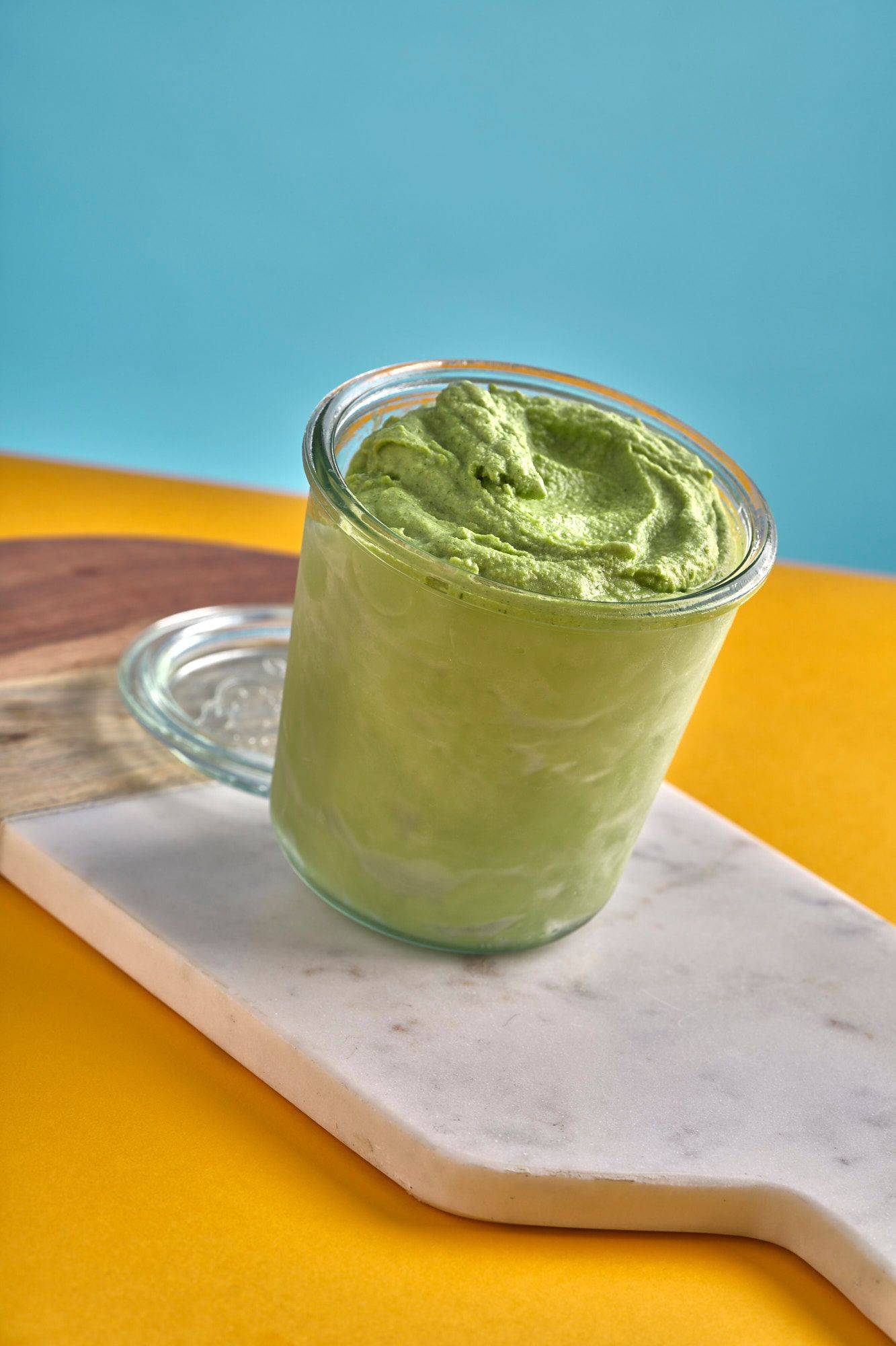 a jar with herbs and yogurt ice cream on a marble board with yellow and blue background