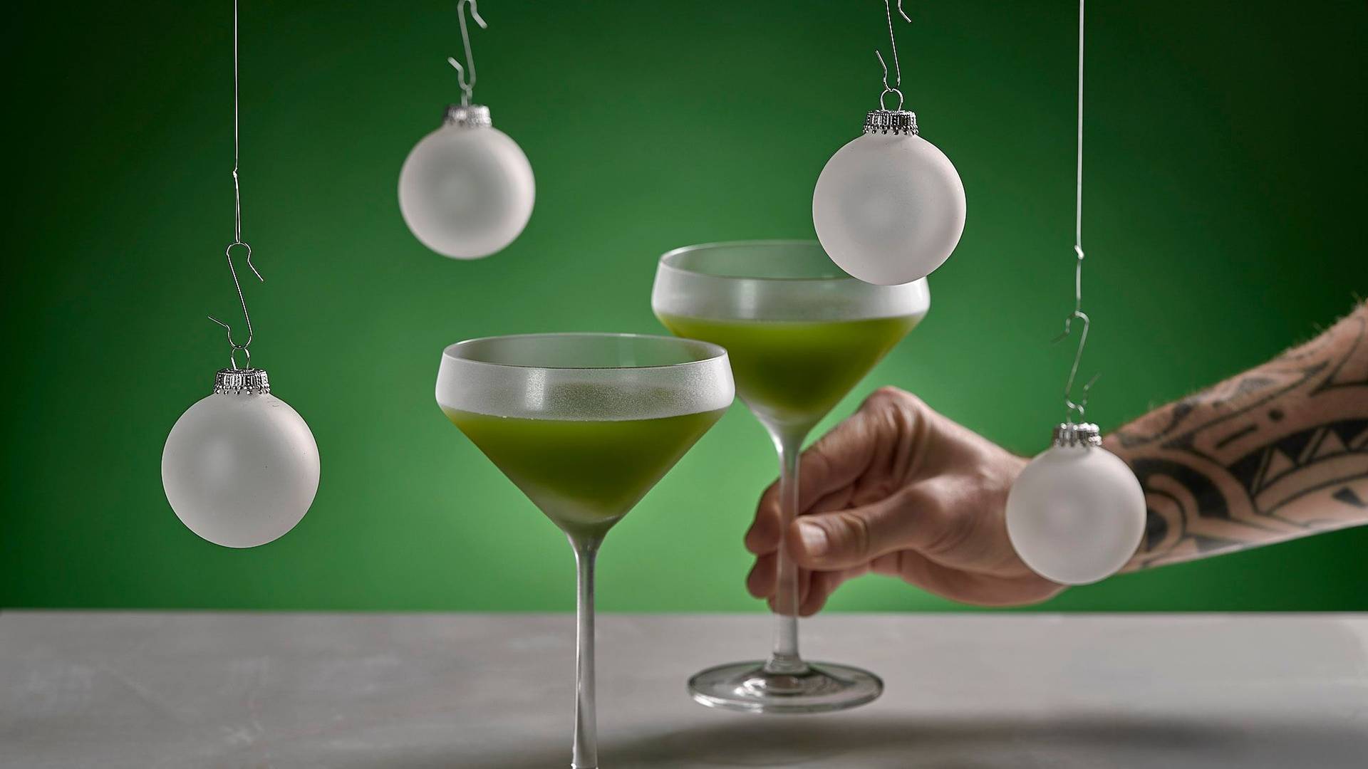 zwei gläser des alkoholfreien grinch weihnachts cocktails auf weißem sapienstone top mit grünem hintergrund