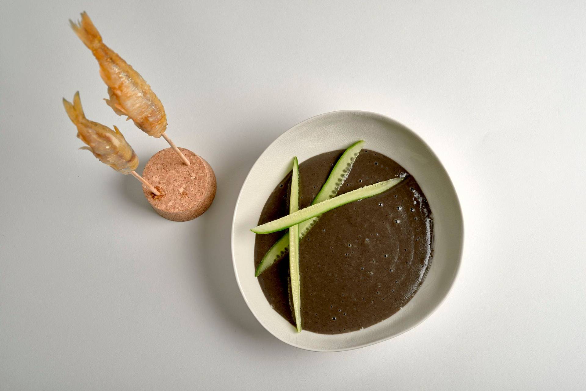 black beluga lentil soup with crispy smelt fish on white background