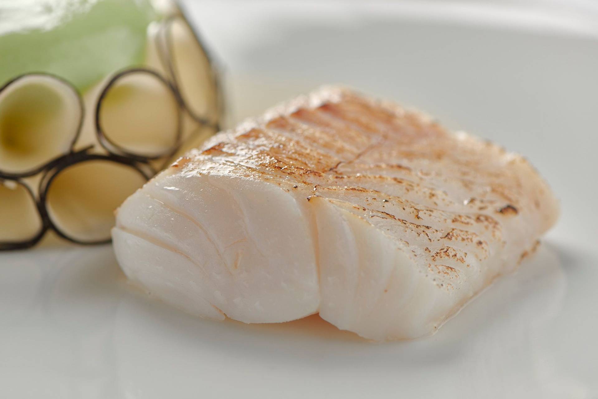 quince poached cod with black radish lovage and chardonnay on a white plate with white background