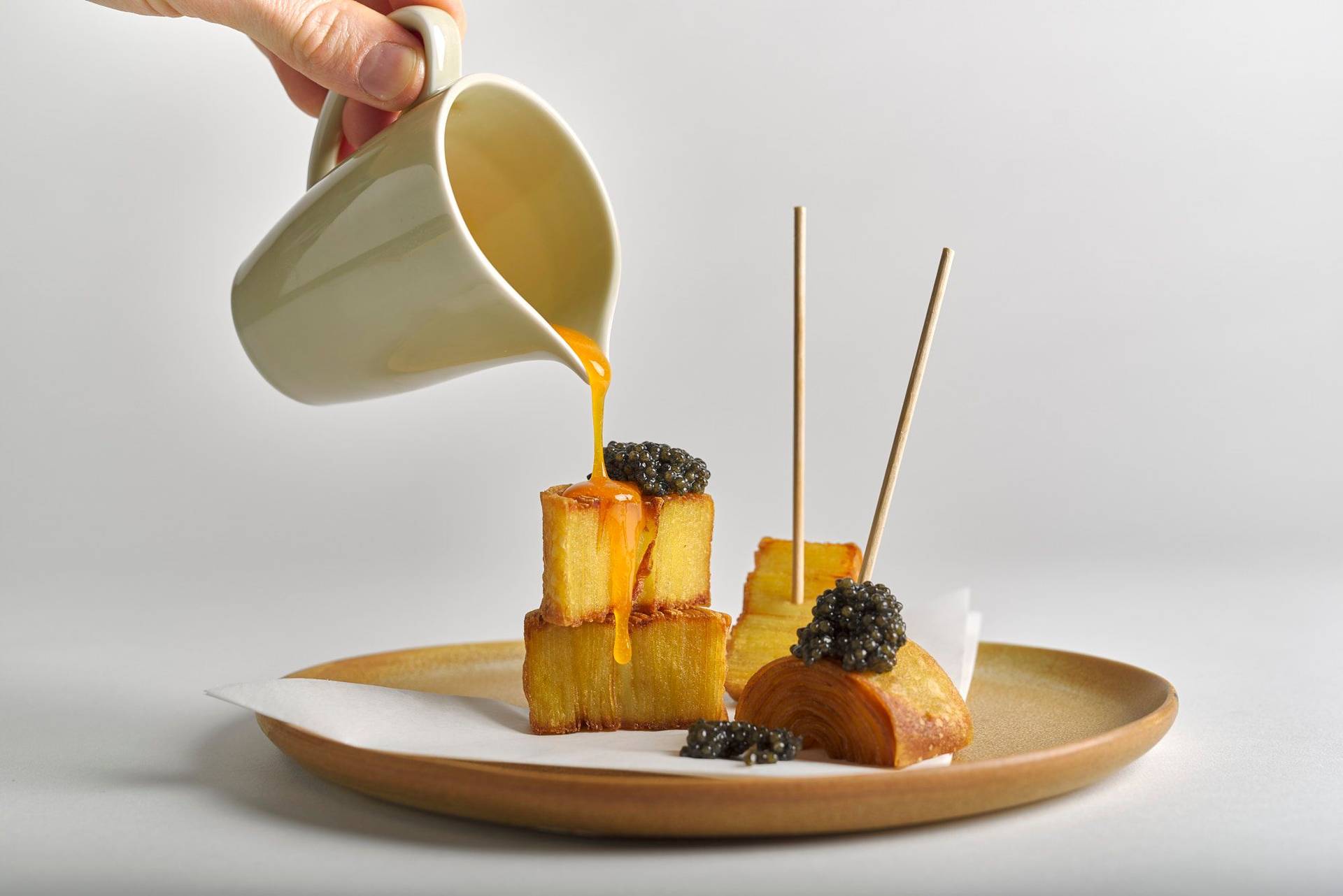 crispy potato swirls with egg yolk and caviar on a brown ceramic plate with white background