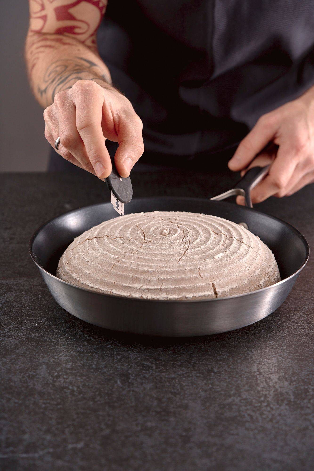 man scoring rye sourdough bread in home kitchen