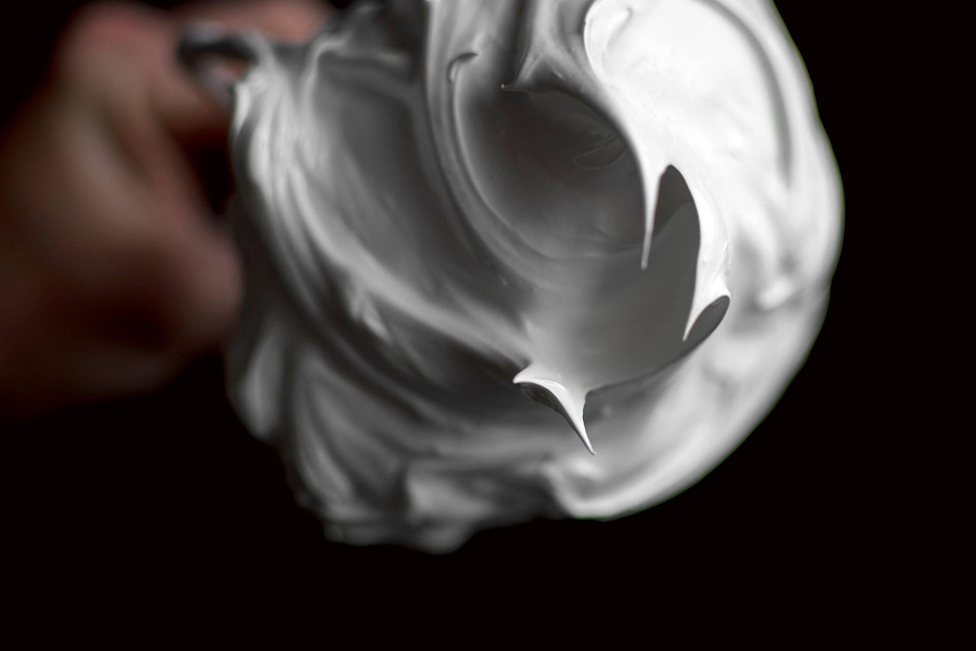 creamy meringue on a whisk with black background