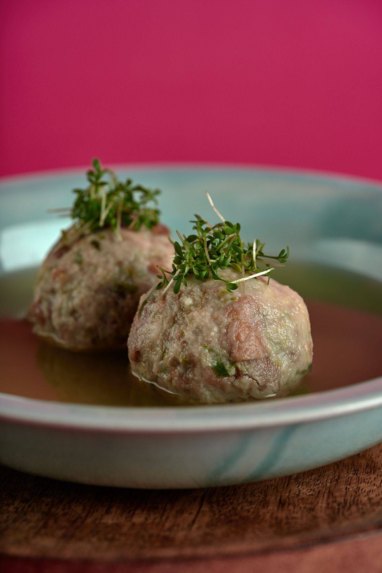 vegan bread dumplings with brussels sprouts and vegetable broth on a turquoise plate with pink background
