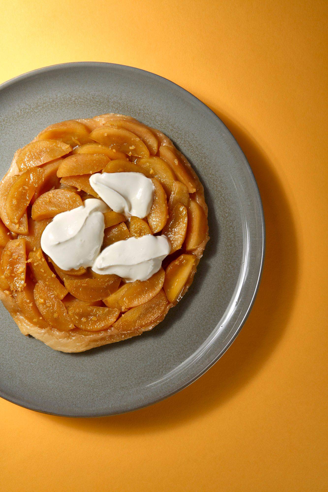 apple and ginger tarte tatin with creme fraiche on a gray plate with yellow background