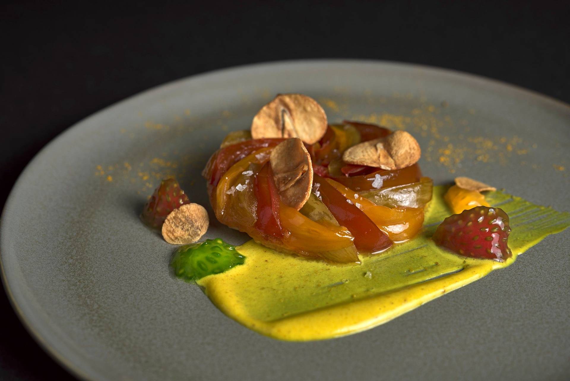 herzhafte tomaten tarte tatin mit curry creme fraiche und knoblauch chips auf einem grauen teller mit schwarzem hintergrund