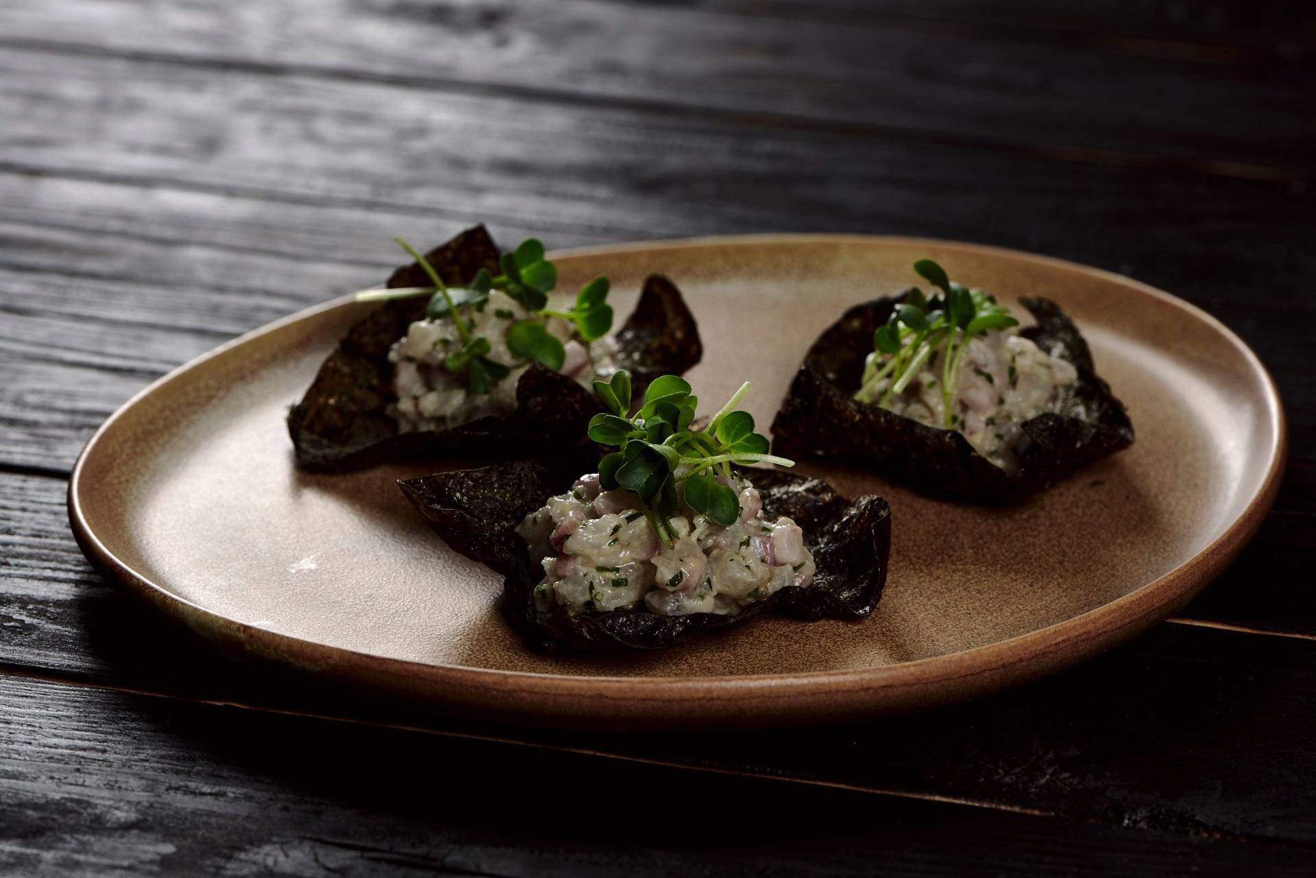 sea bass tartare with nori cracker on a brown ceramic plate with black wooden background