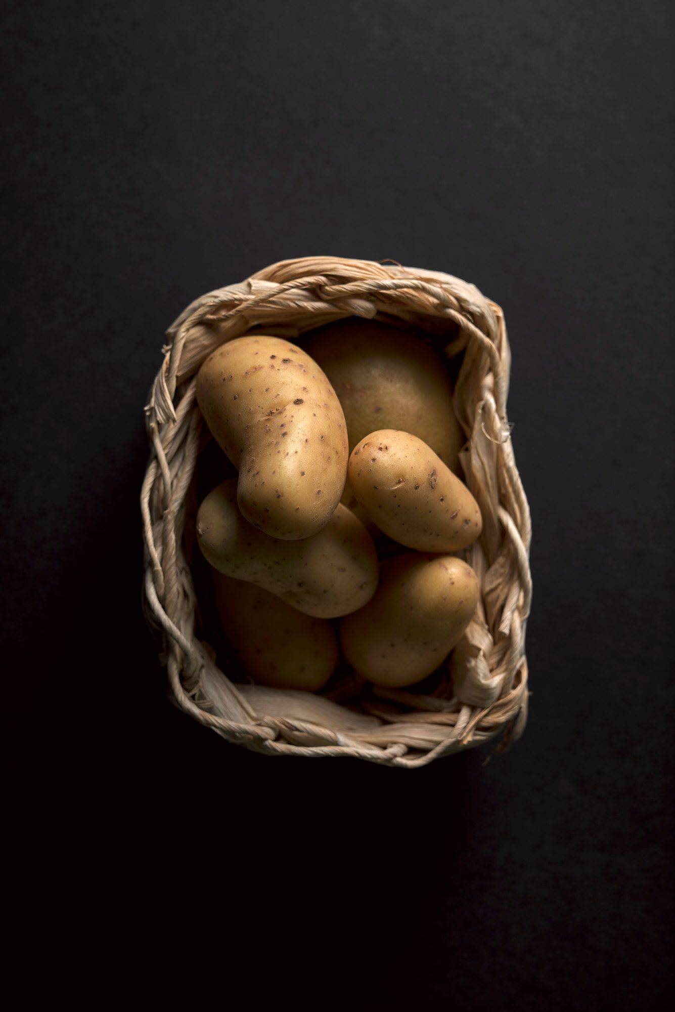 kartoffeln in einem kleinen bastkörbchen auf schwarzem hintergrund