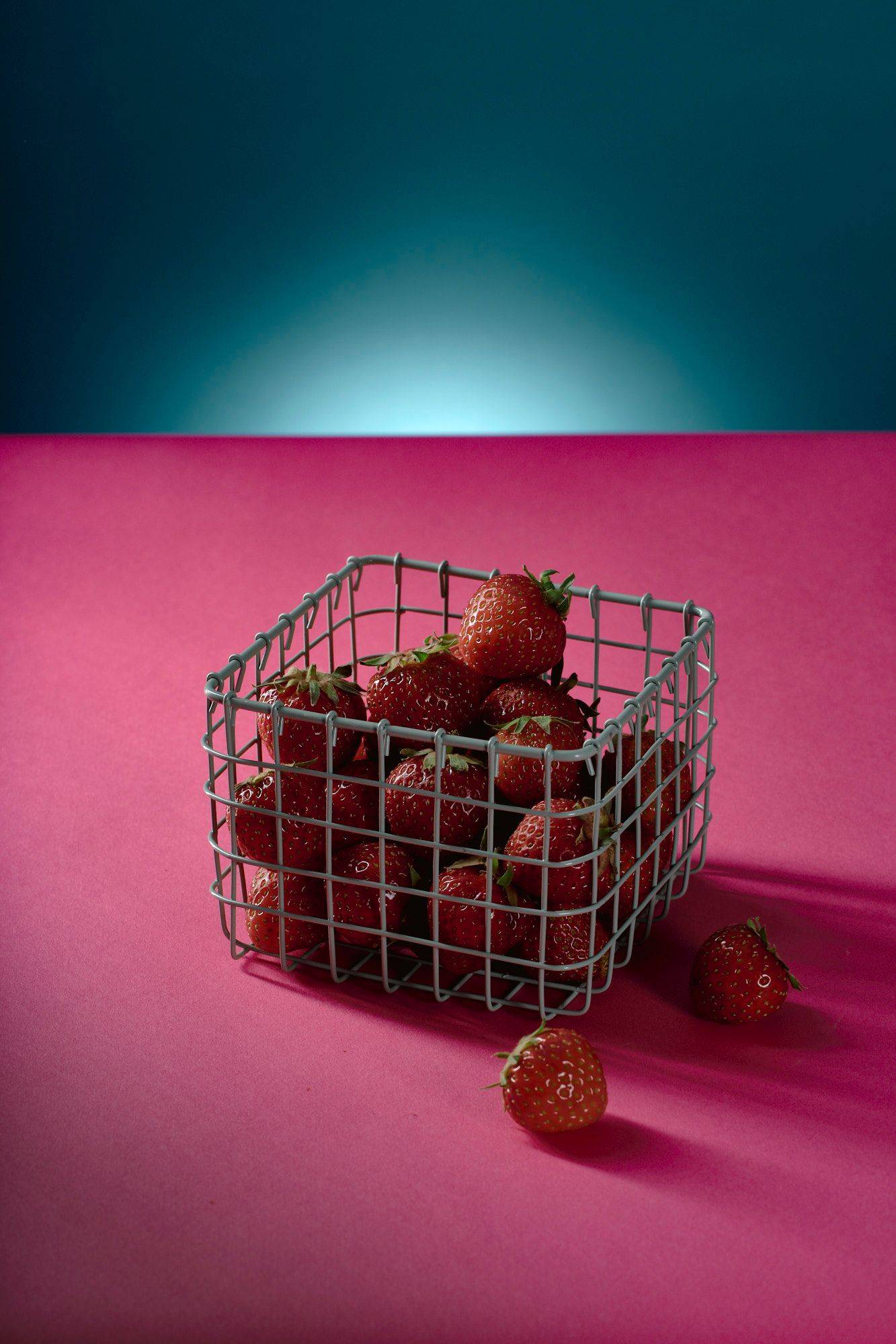 a small basket of strawberries with pink and blue background