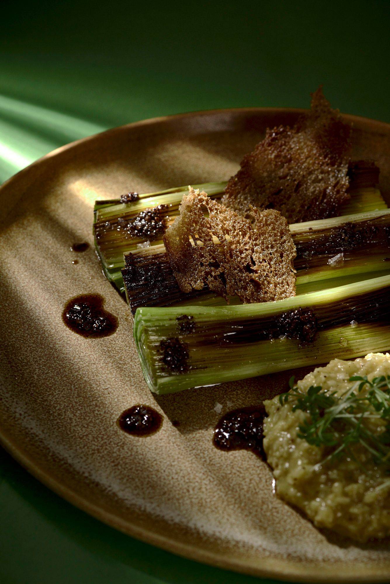 roasted leek with passion fruit porridge and coffee breakfast on a brown ceramic plate with green background