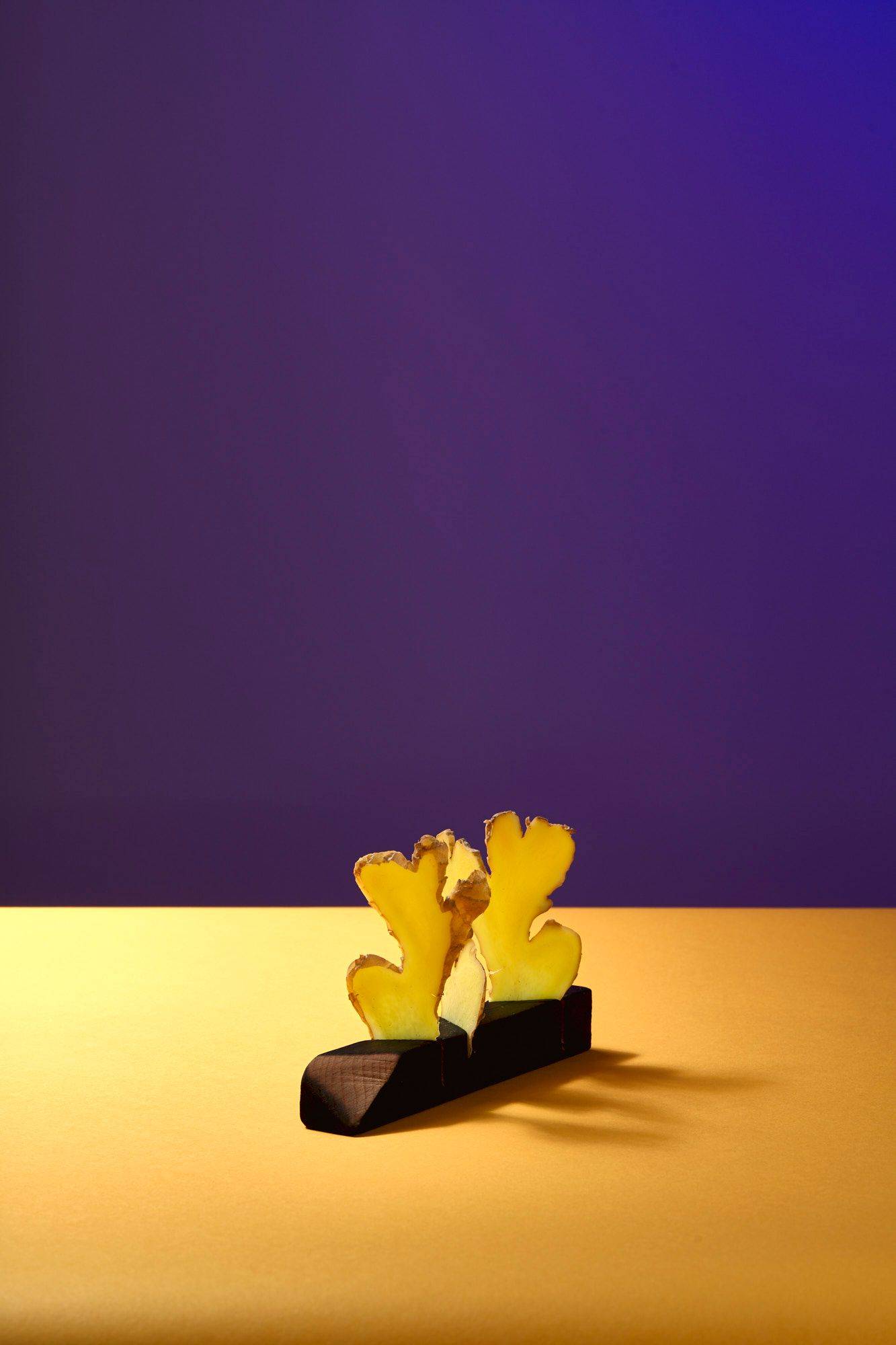 three slices of ginger on a wooden stand with yellow and purple background