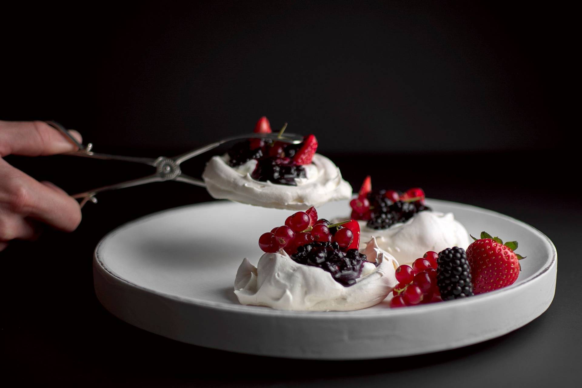 pavlova mit beeren und salziger sahne auf einem weißen holzteller mit schwarzem hintergrund