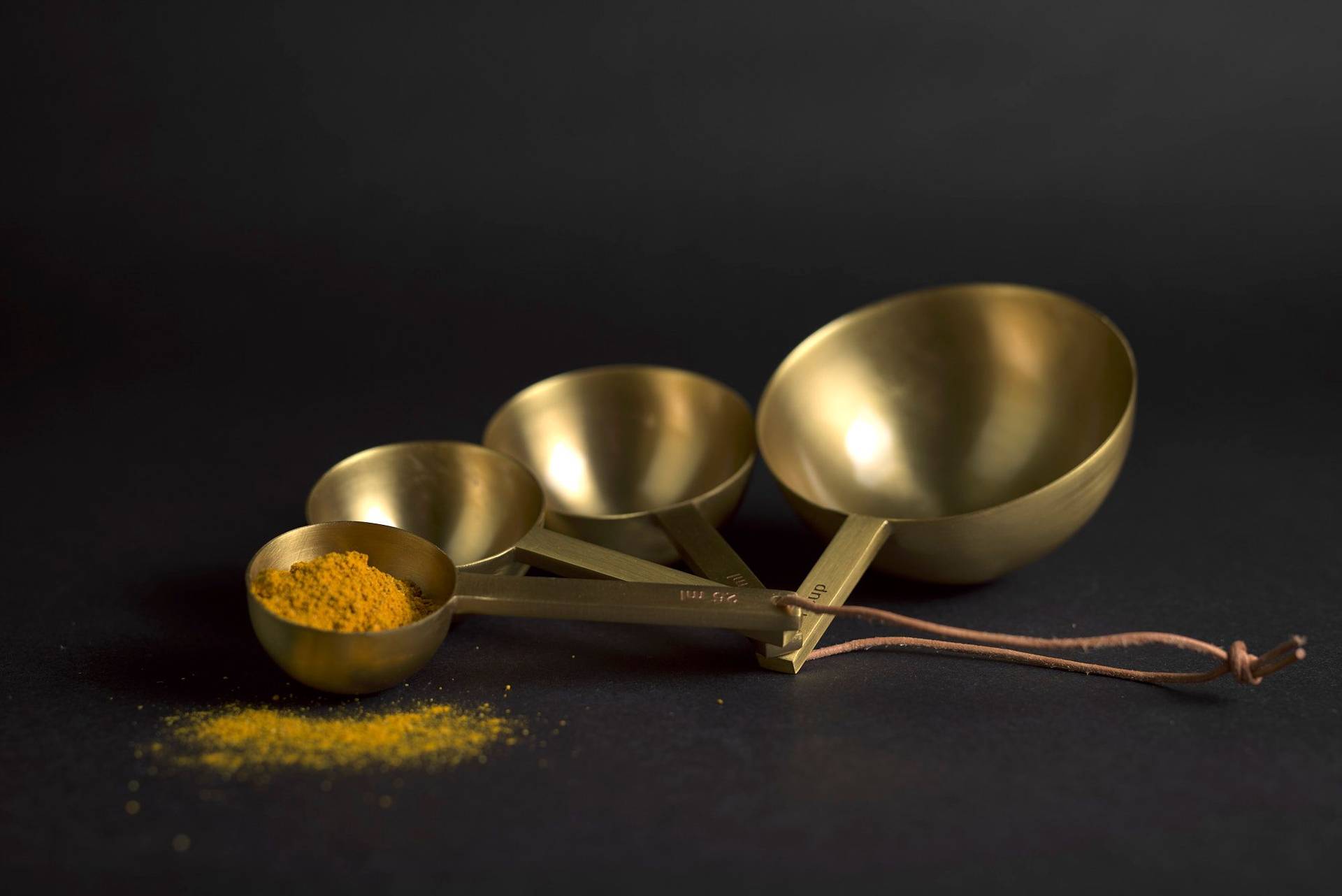 madras curry powder in brass measuring spoons with black background