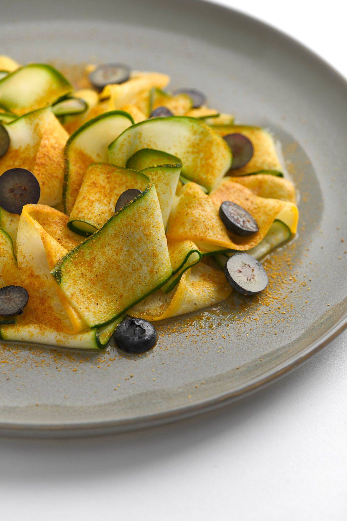 courgette with almond butter madras curry and blueberries on a gray plate with white background