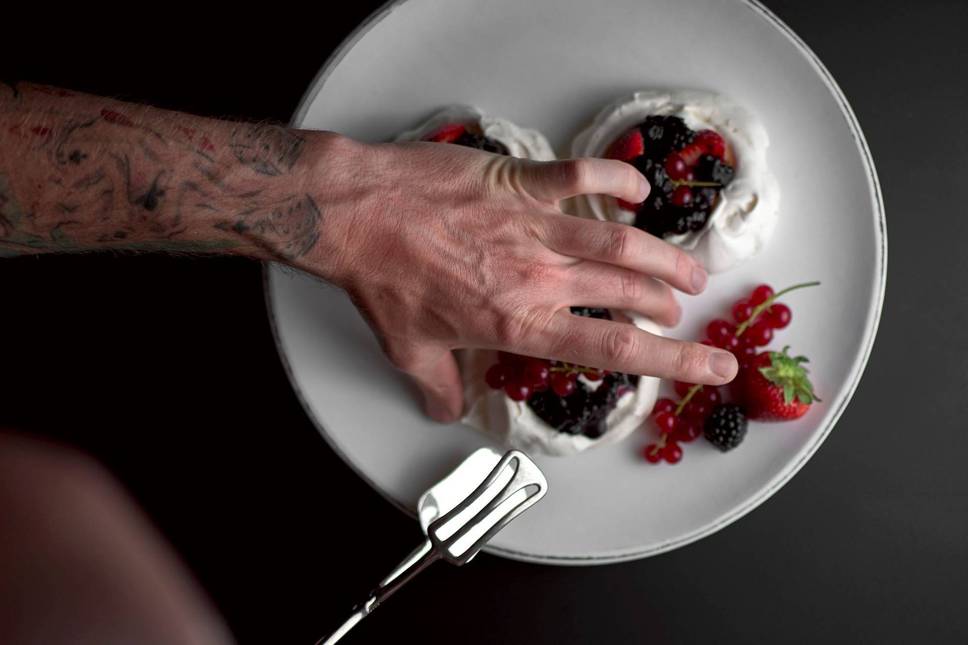 pavlova mit beeren und salziger sahne auf einem weißen holzteller mit schwarzem hintergrund