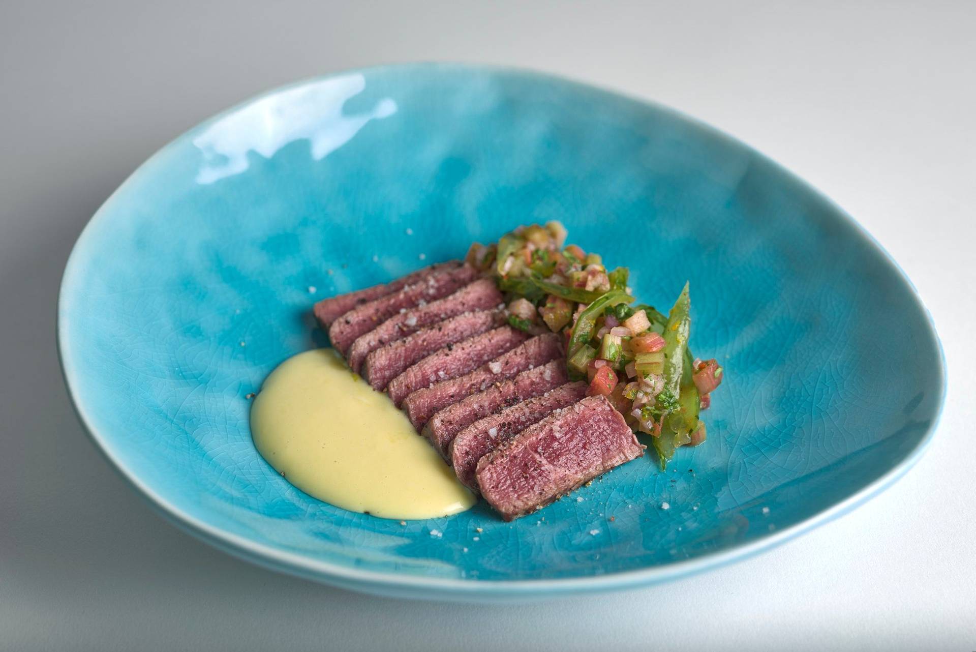 beef tataki with tomato salsa and ginger mayonnaise on a turquoise plate with white background
