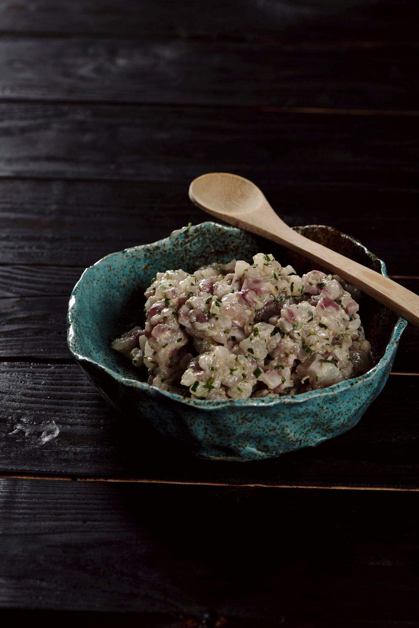 sea bass tartare in a turquoise ceramic bowl with black wooden background