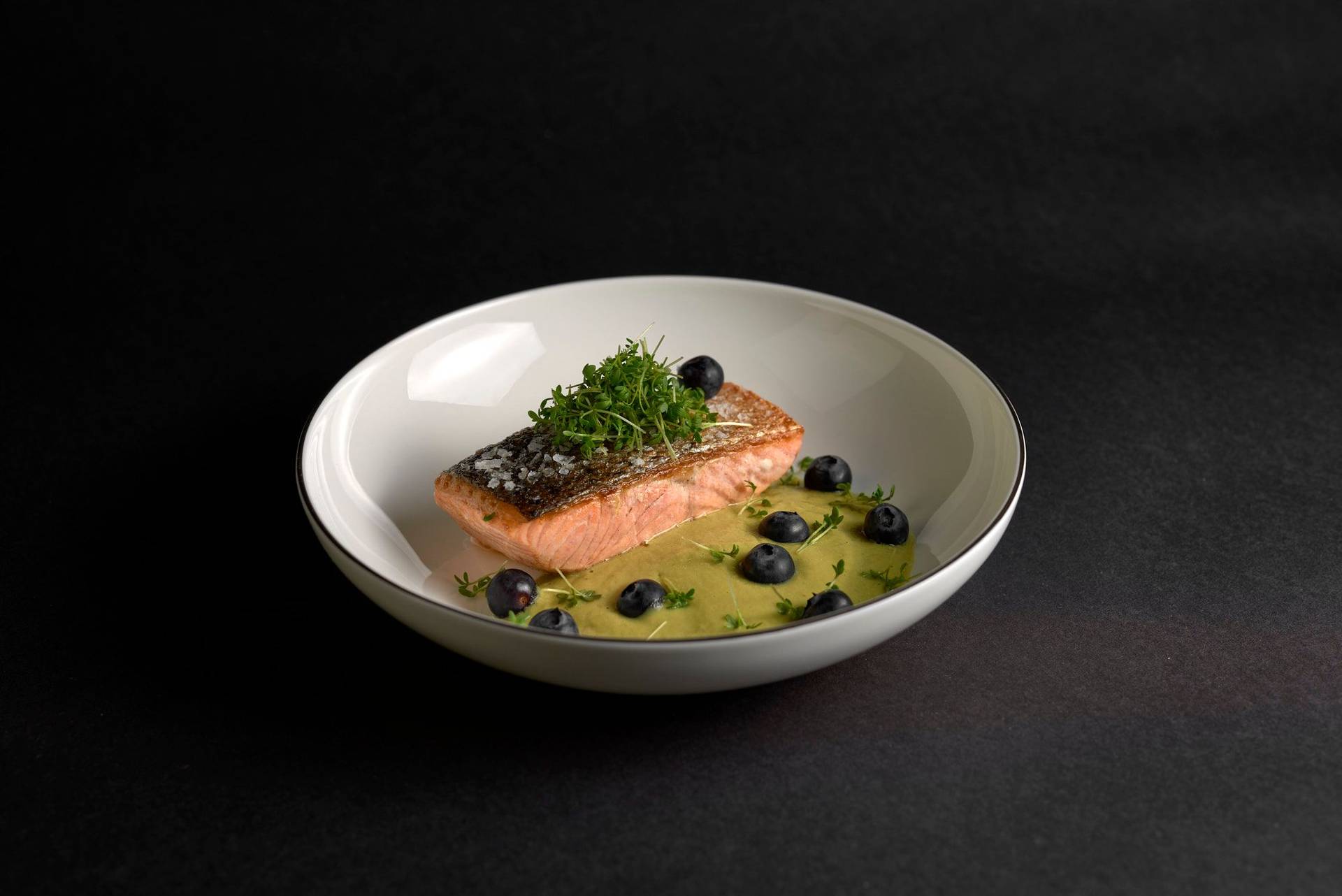 pan fried salmon with asparagus matcha sauce and blueberries on a white plate with black background