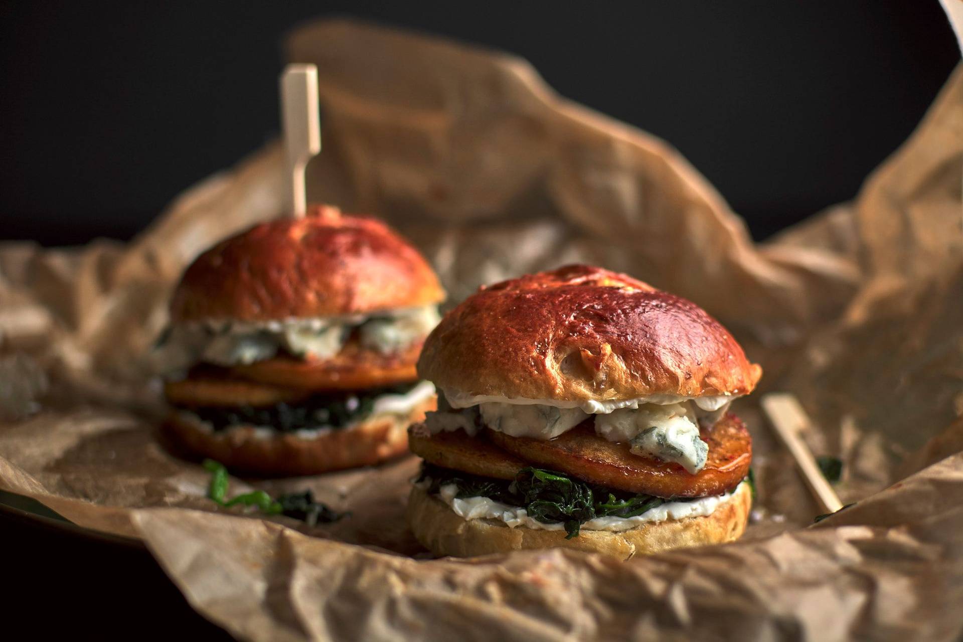vegetarischer Kürbis-Brioche Burger mit Blauschimmel Käse und Spinat vor schwarzem Hintergrund