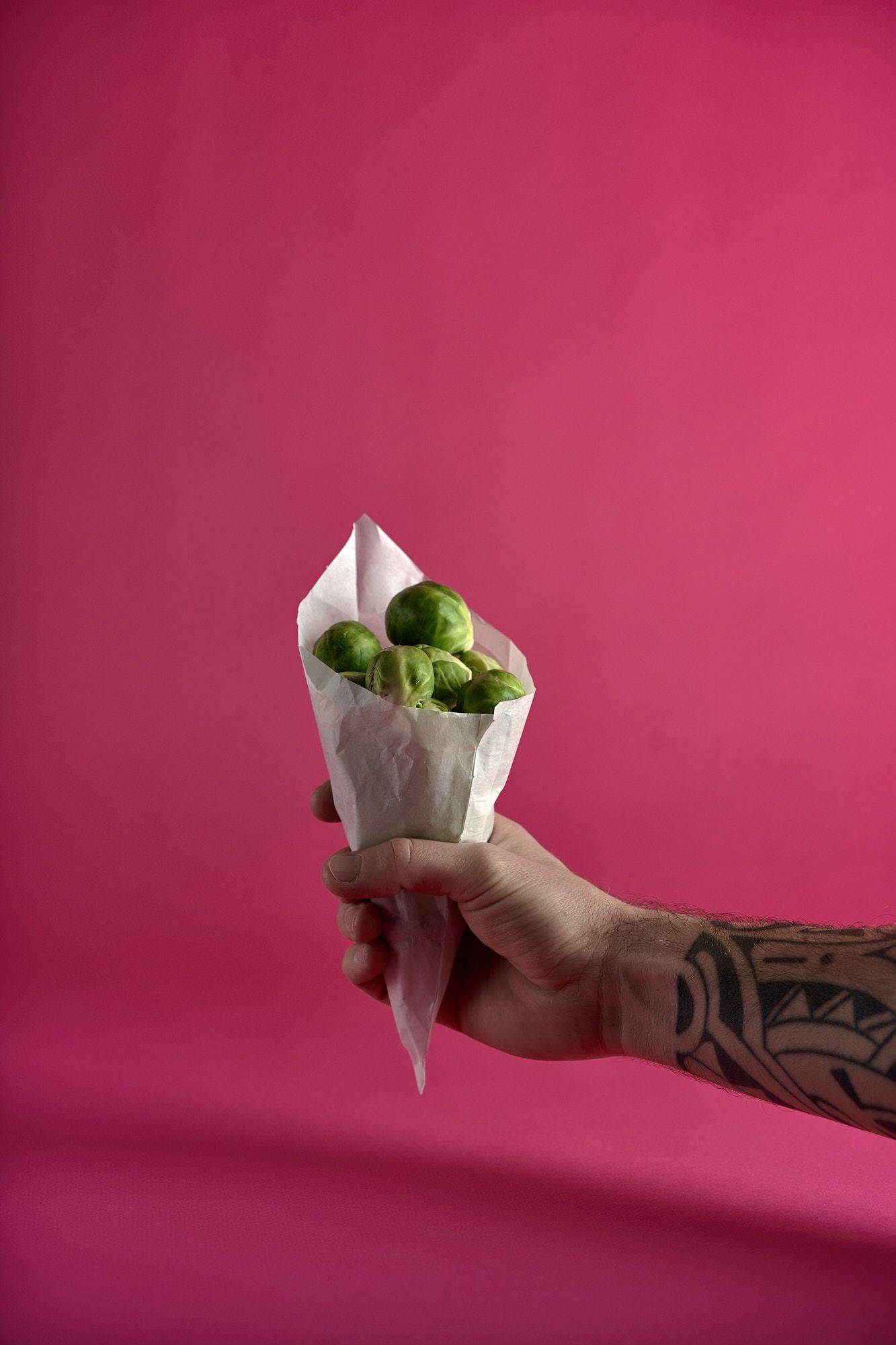 eine hand hält eine papiertüte mit rosenkohl vor pink hintergrund