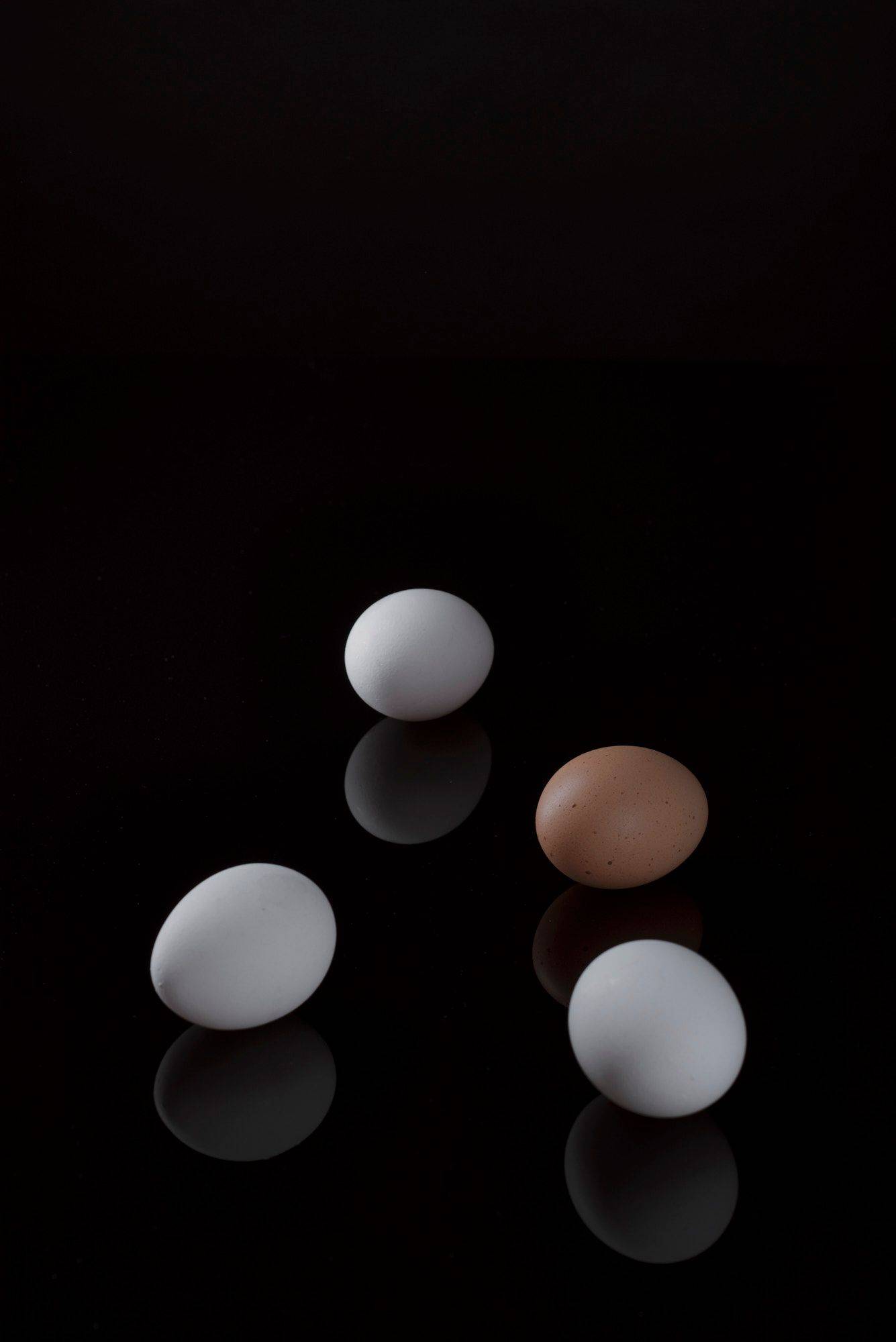 three white and one brown egg with black background