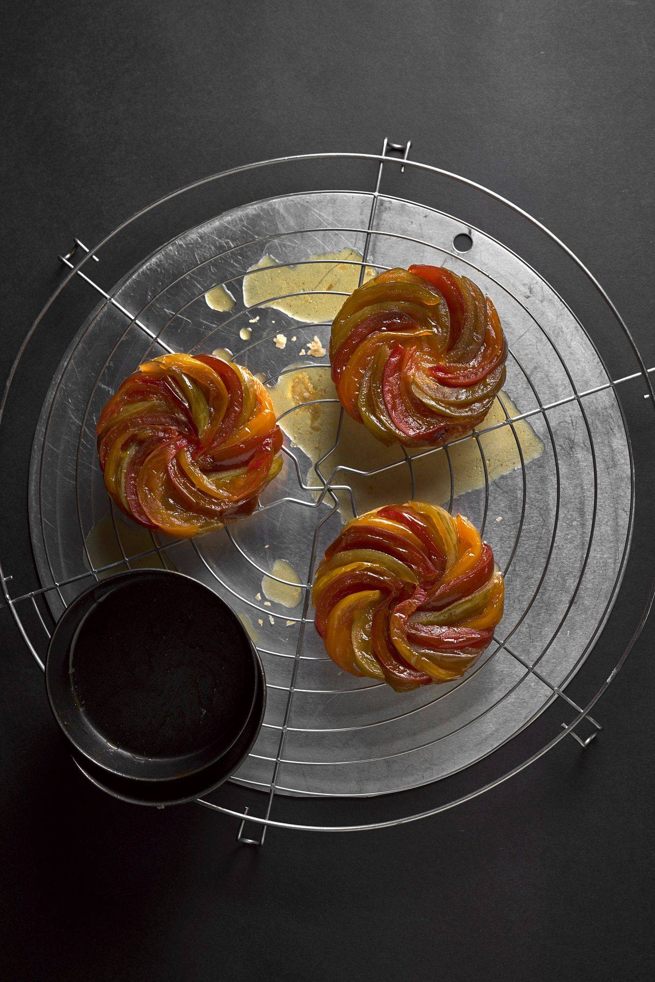 three freshly baked tomato tarte tatins on a baking grid with black background