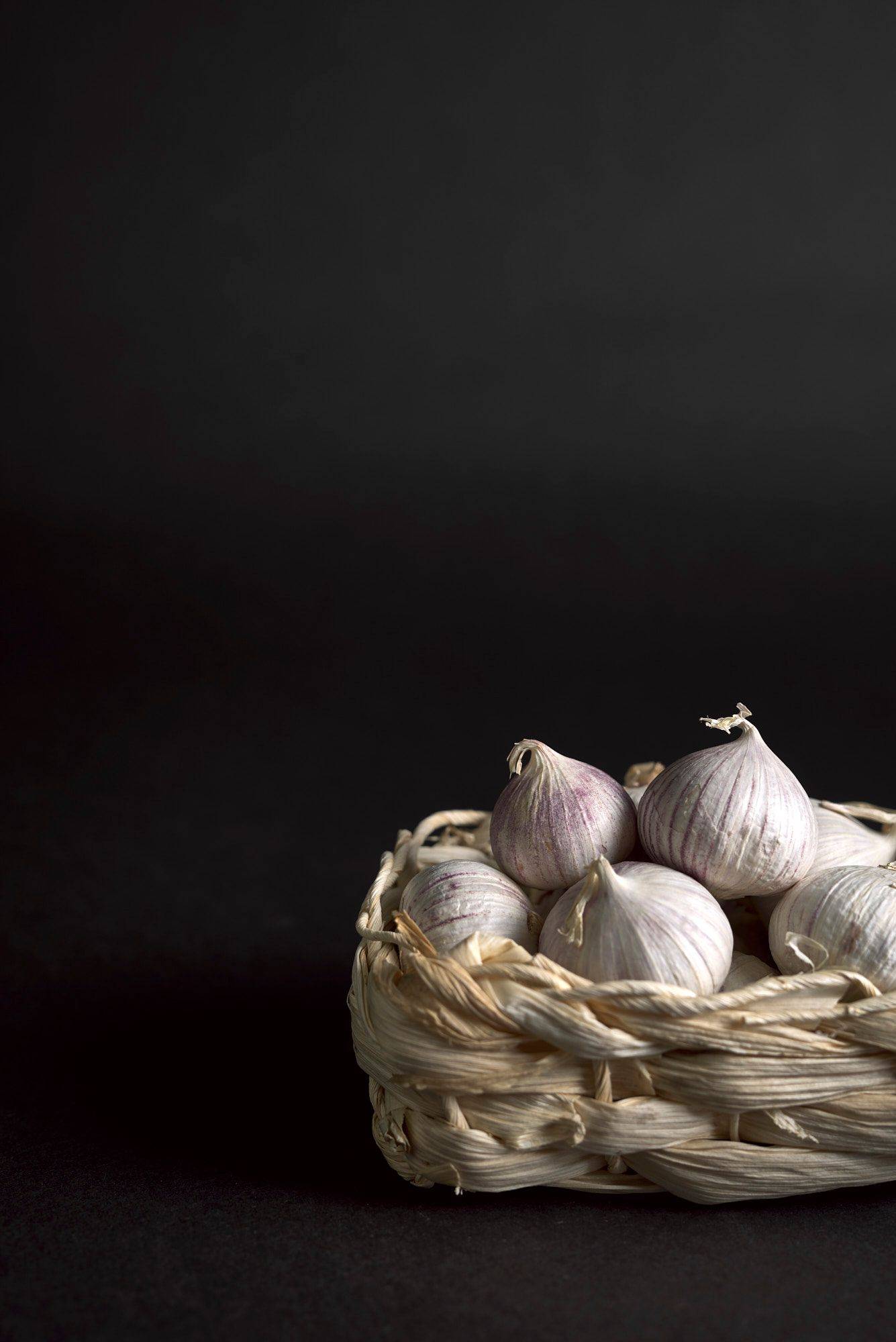 knoblauch in einem kleinen bastkörbchen mit schwarzem hintergrund