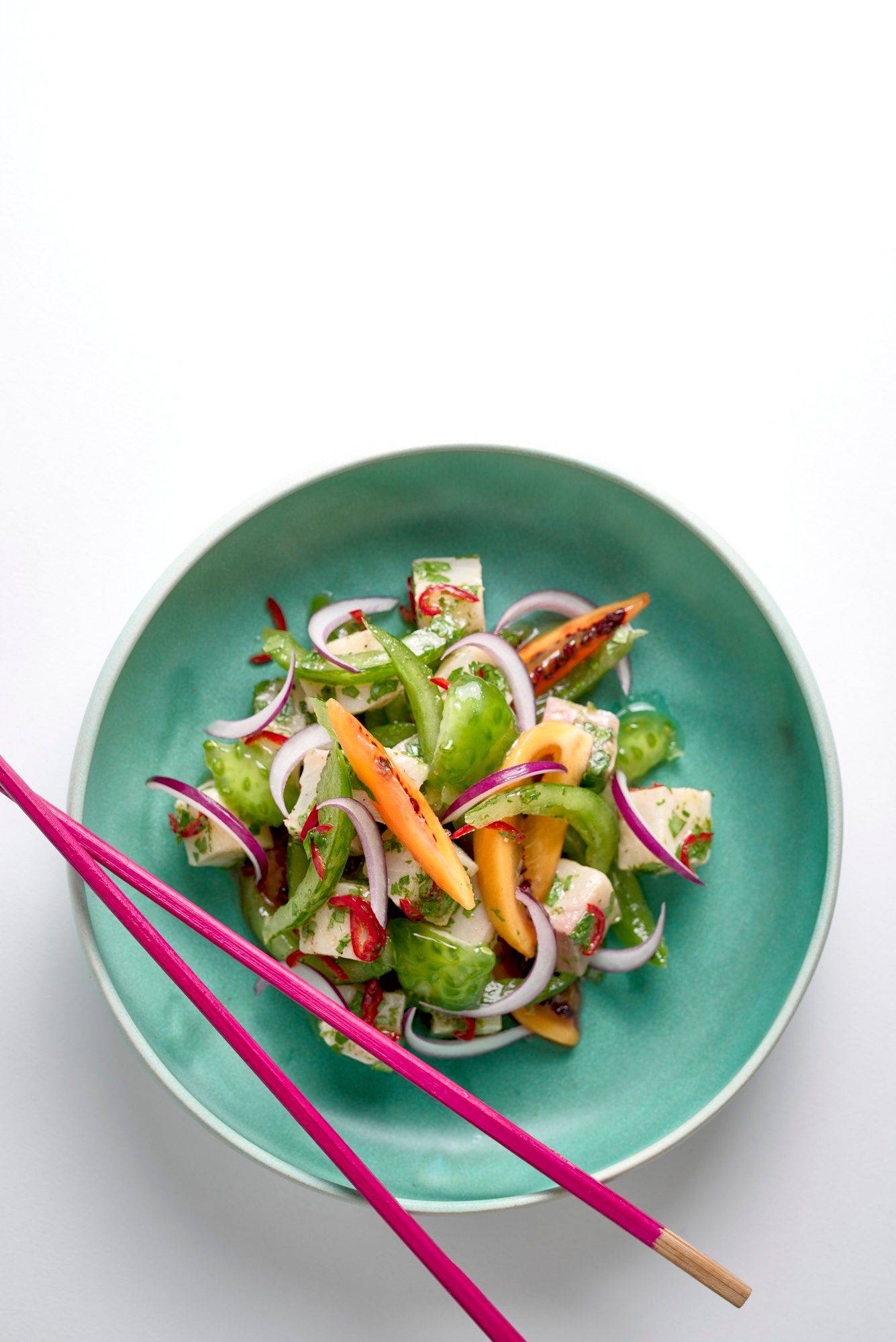 kingfish ceviche with tomatoes in a turquoise ceramic bowl on white background