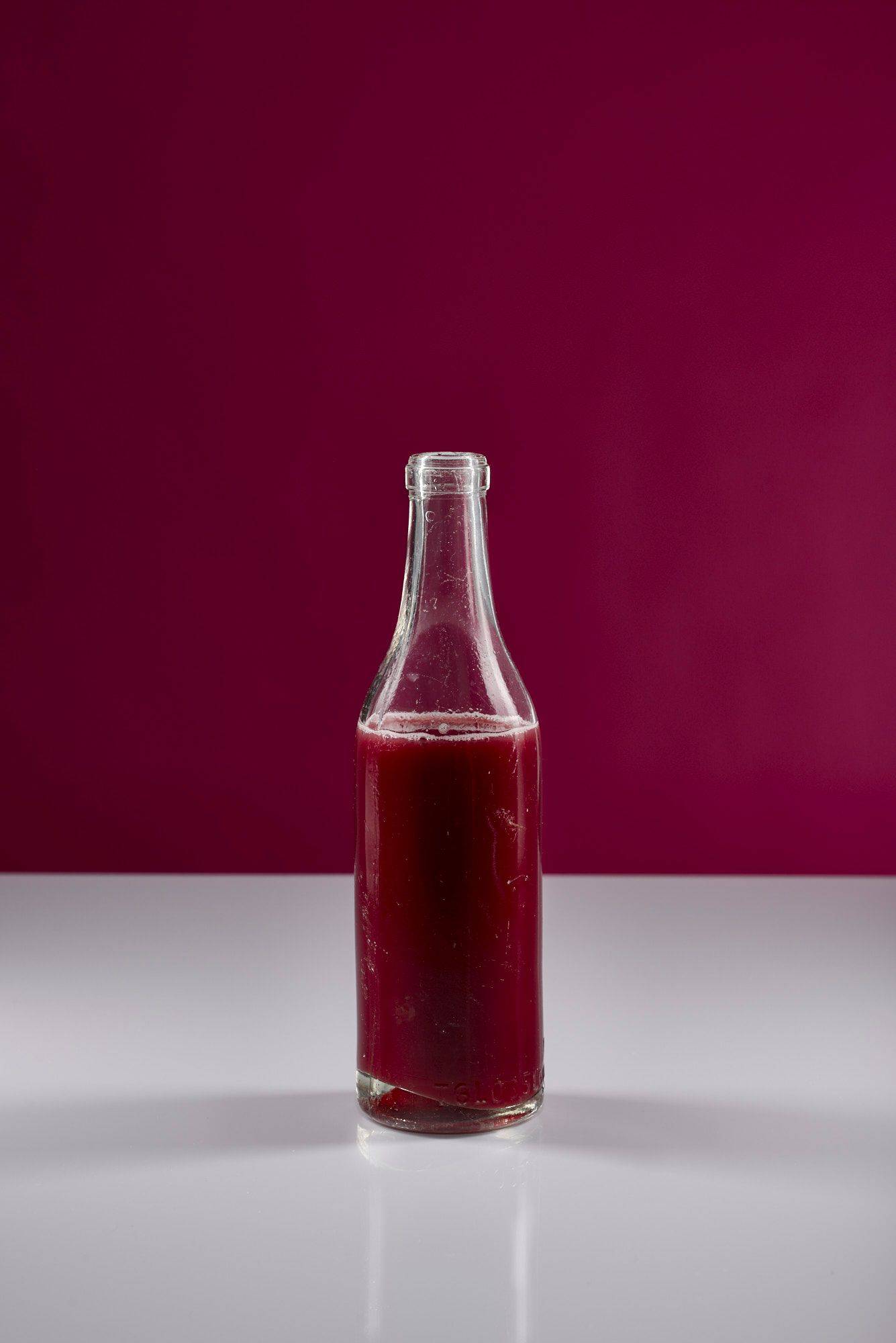 a glass bottle of pomegranate juice with white and pink background