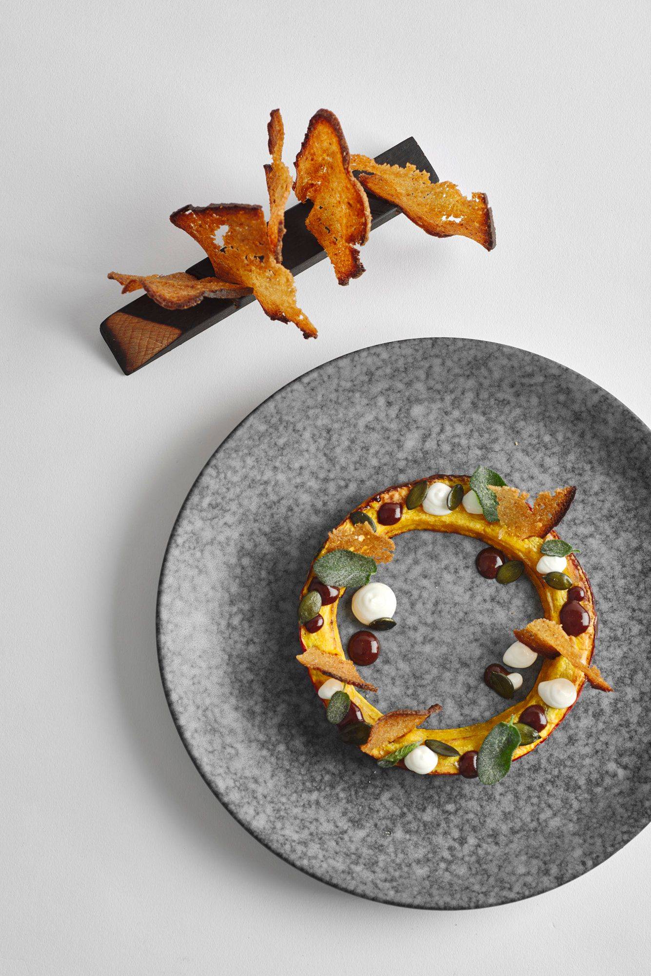 kürbis variation mit salbei und sauerteigbrot auf eienm grauen teller mit weißem hintergrund