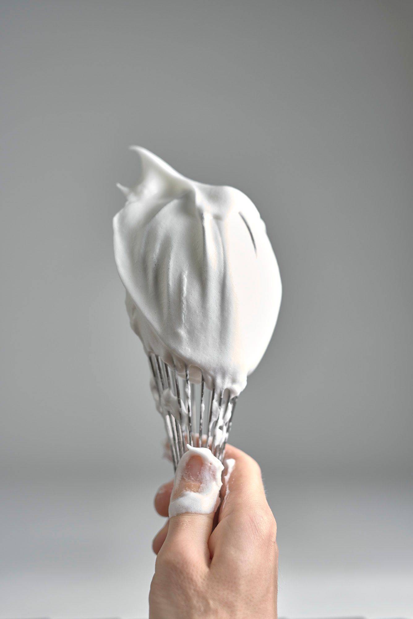 hand holds a whisk with fluffy meringue with white background
