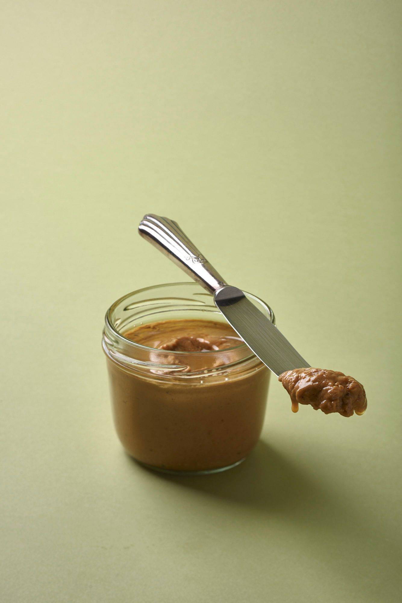 a jar with roasted almond butter with green background
