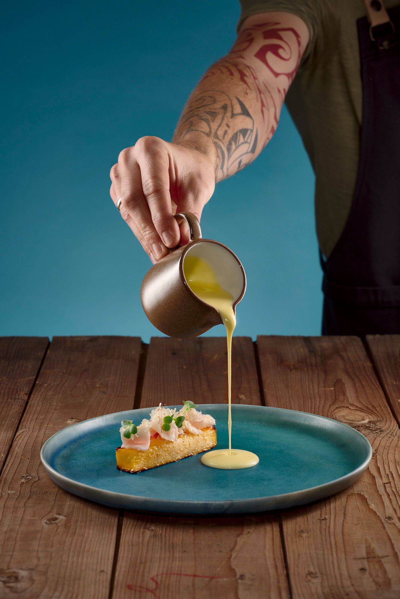 rutabaga with lardo bacon and beurre blanc of pickled gherkins on a blue plate with wooden table and blue background