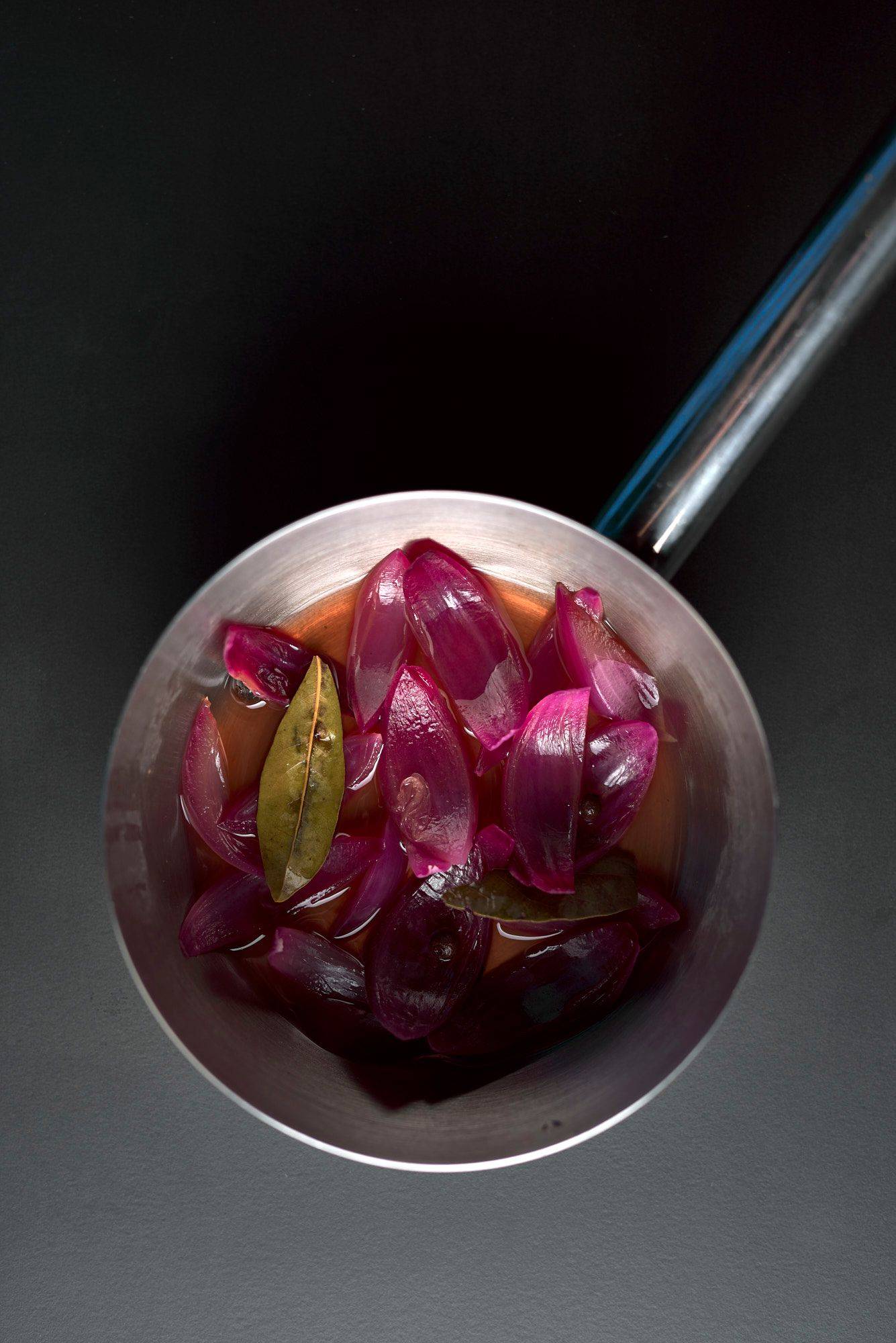 red onion pickles in a metal pot on black background