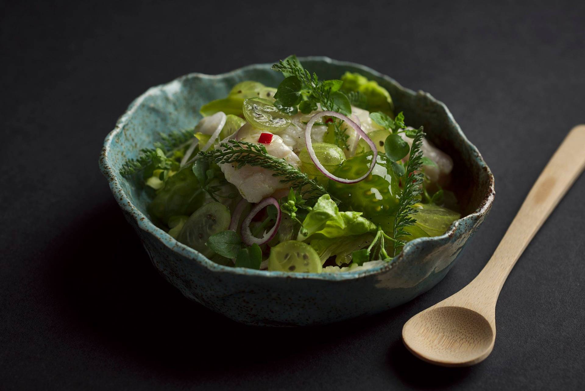 cod ceviche with gooseberries in a turquoise ceramic bowl with black background