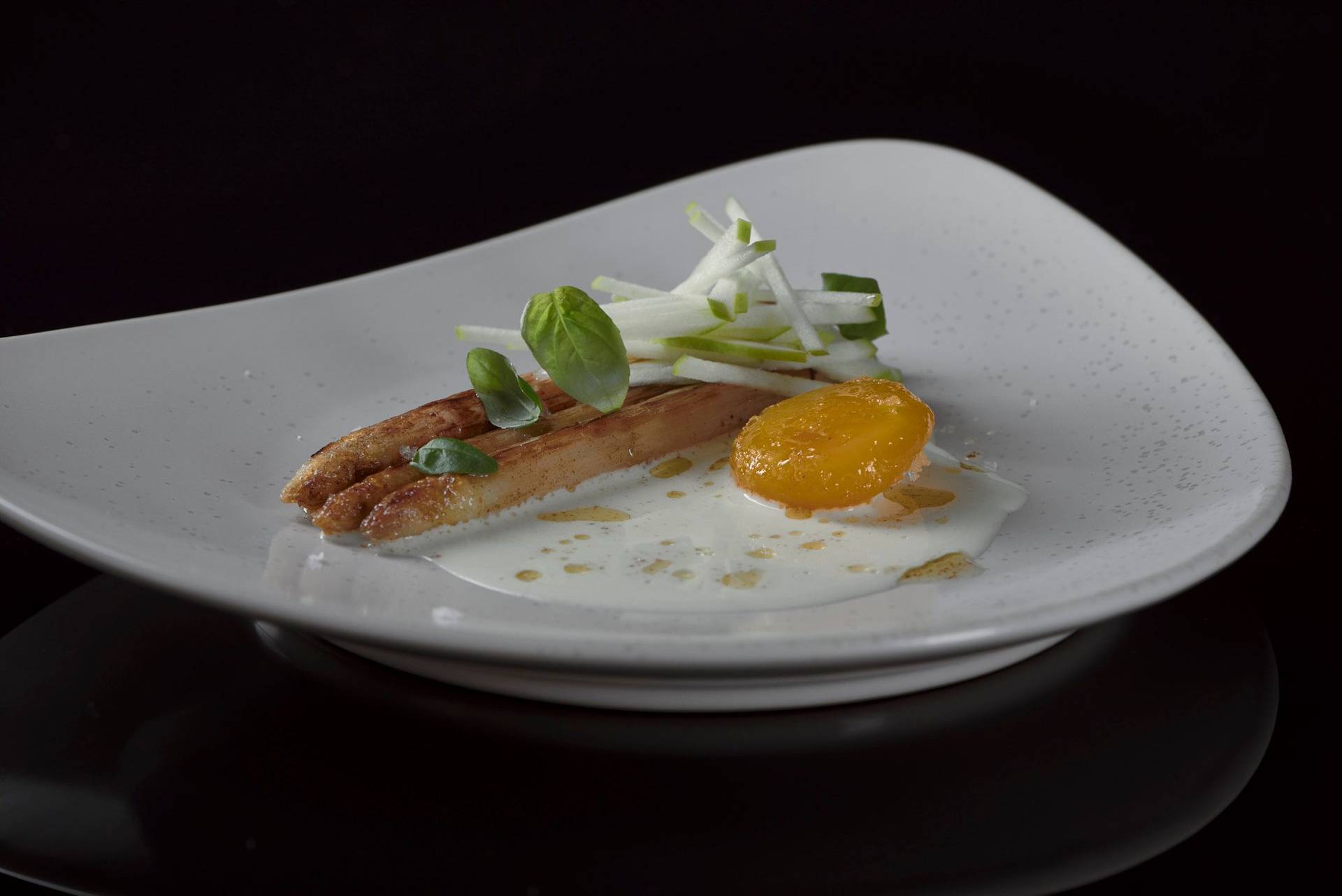 roasted white asparagus with cured egg yolk basil and green apple on a beige plate with black background