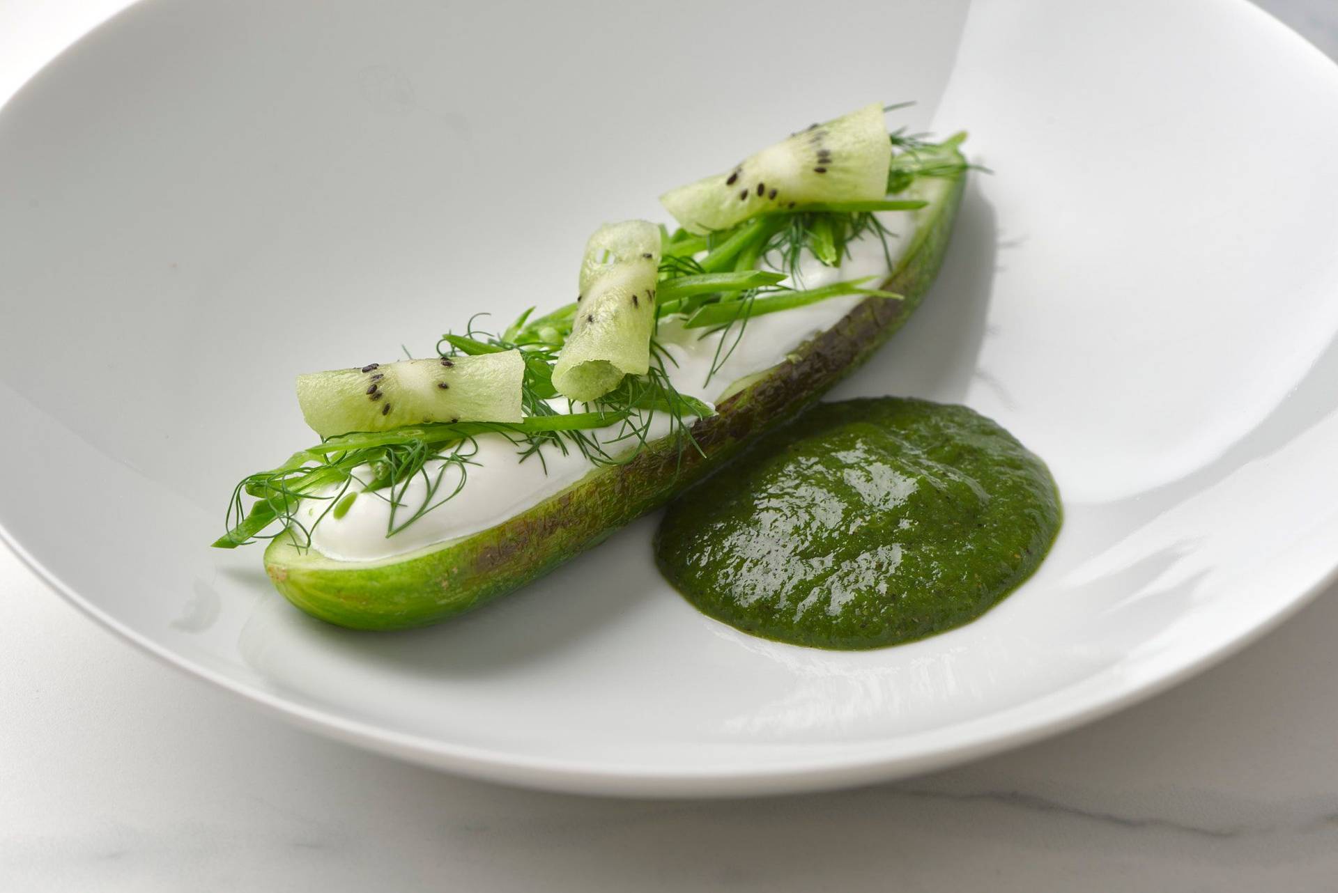 charred cucumber with kiwi salsa skyr and dill on a white plate with a marbled sapienstone top