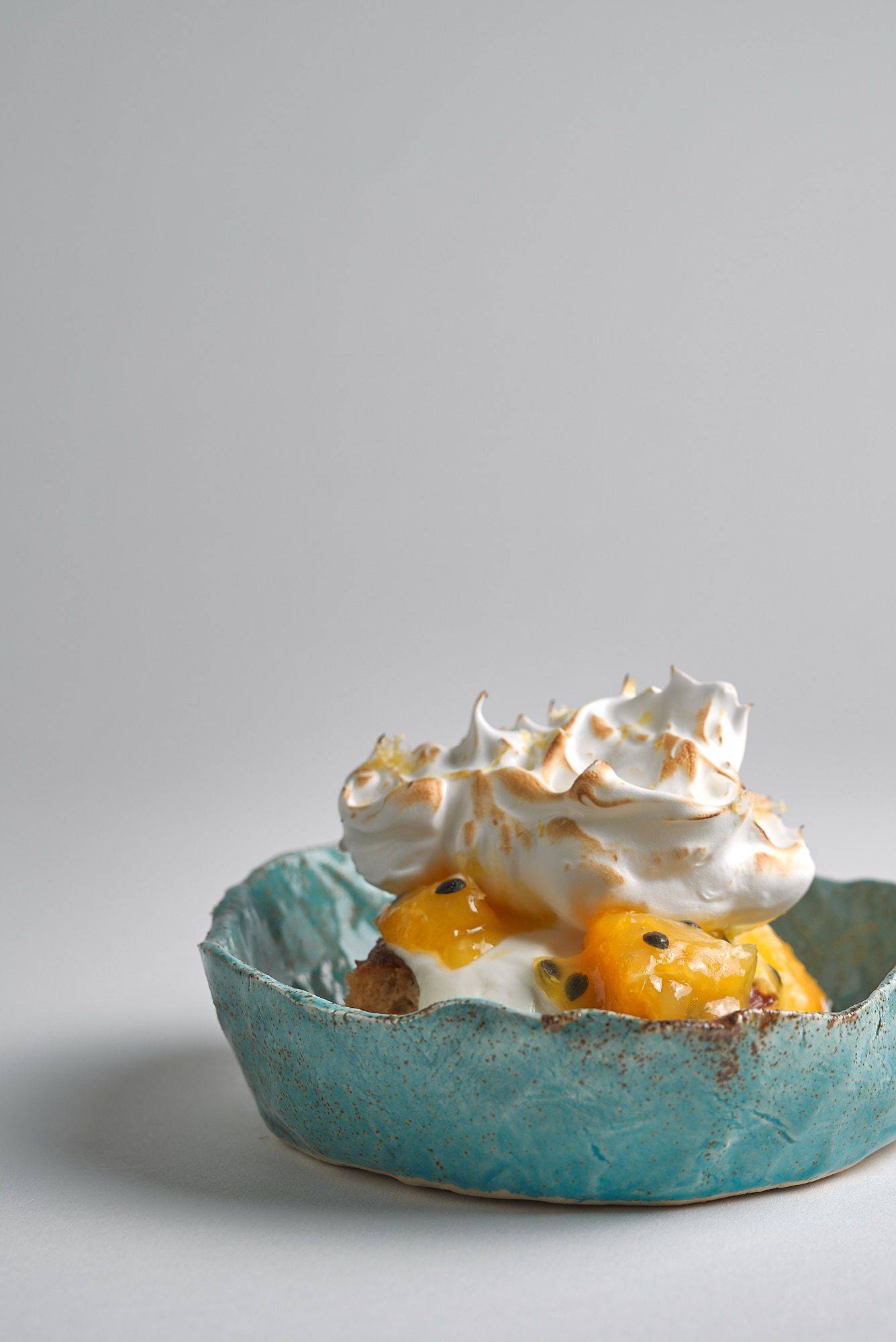 Passionsfrucht Baiser Dessert in blauer Keramikschale vor weißem Hintergrund