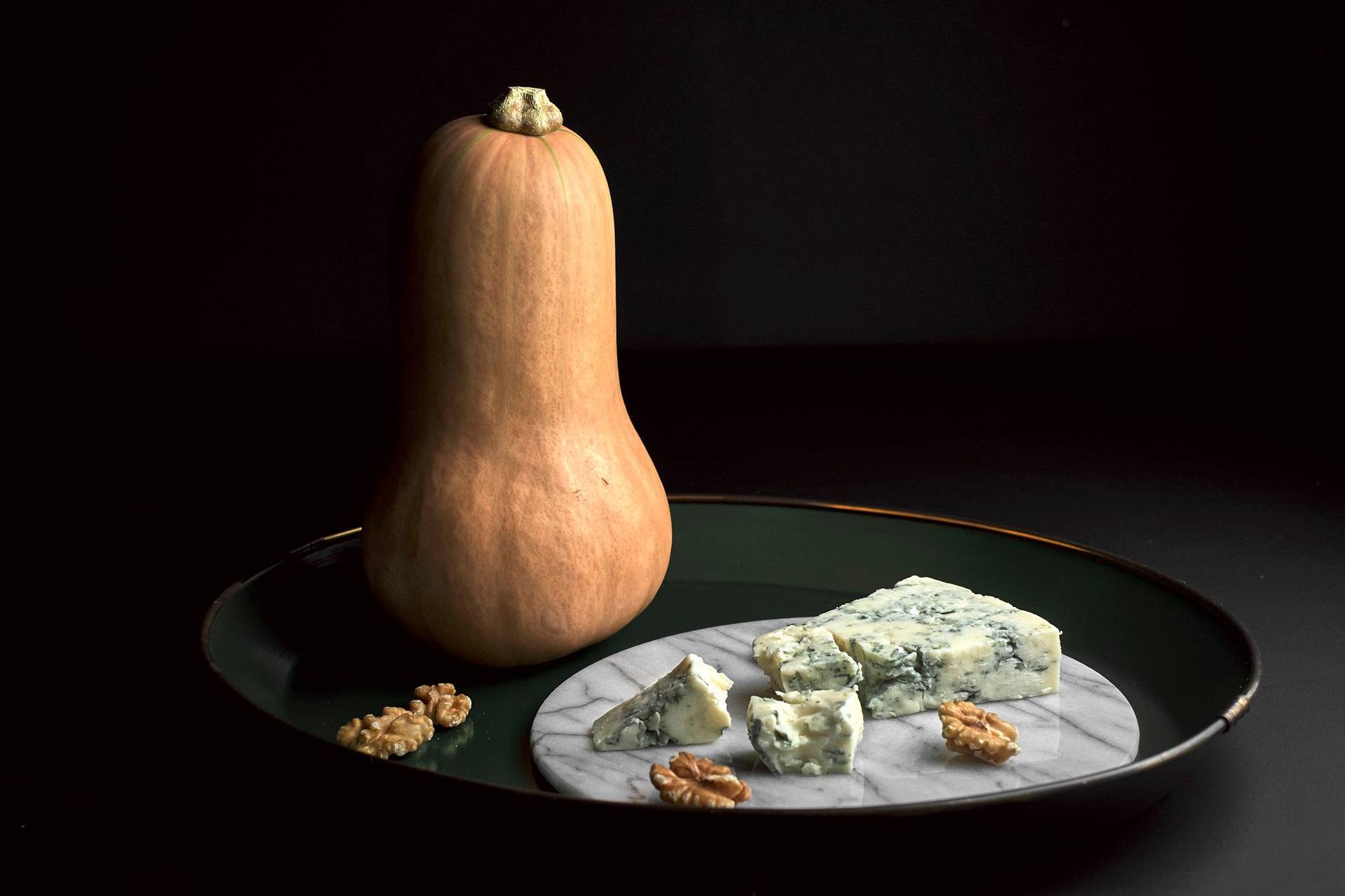 Kürbis, Blauschimmel Käse und Walnüsse auf grünem Tablett mit schwarzem Hintergrund