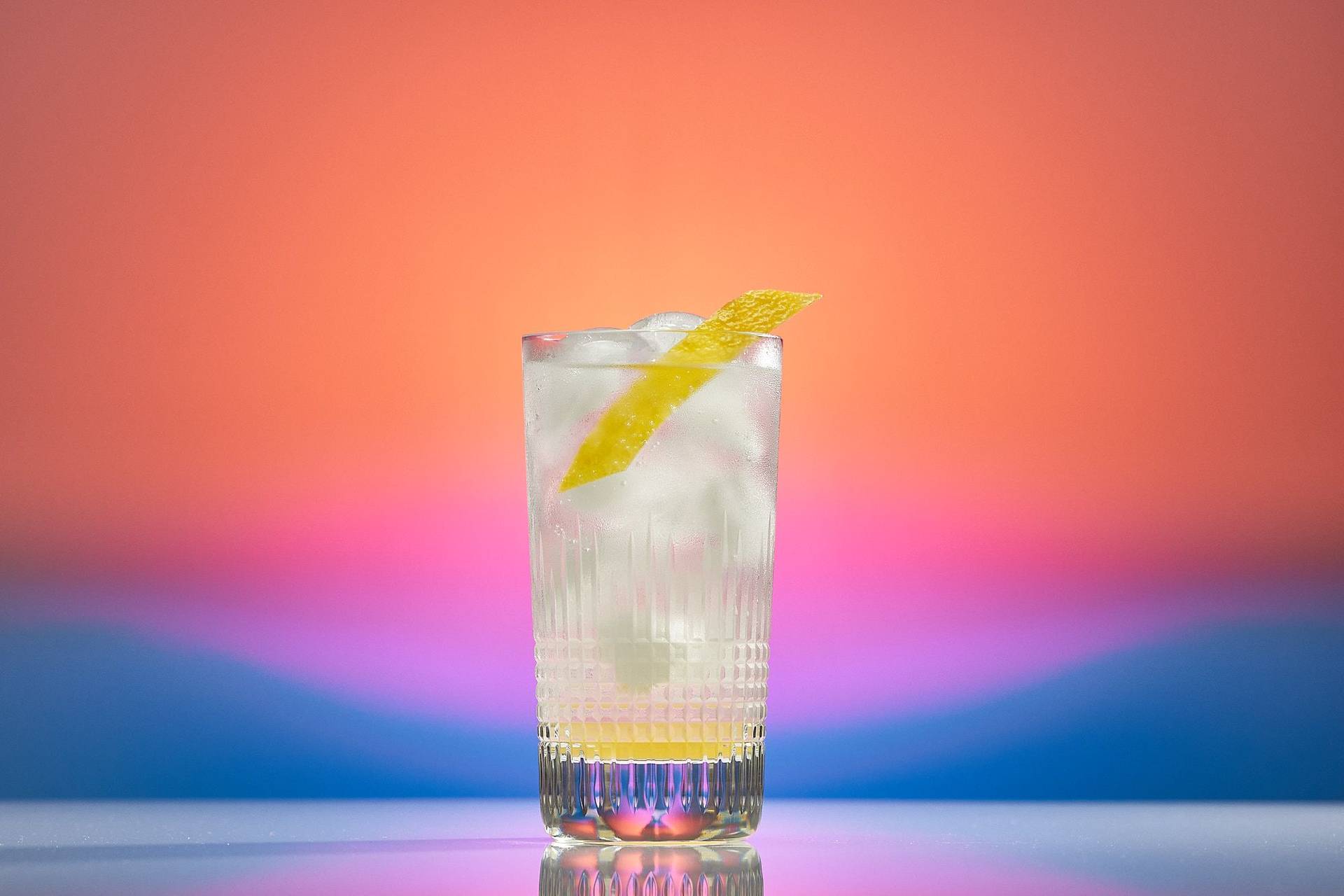 ein glas mit alkoholfreiem ingwer-zitronen cocktail vor regenbogenfarben hintergrund