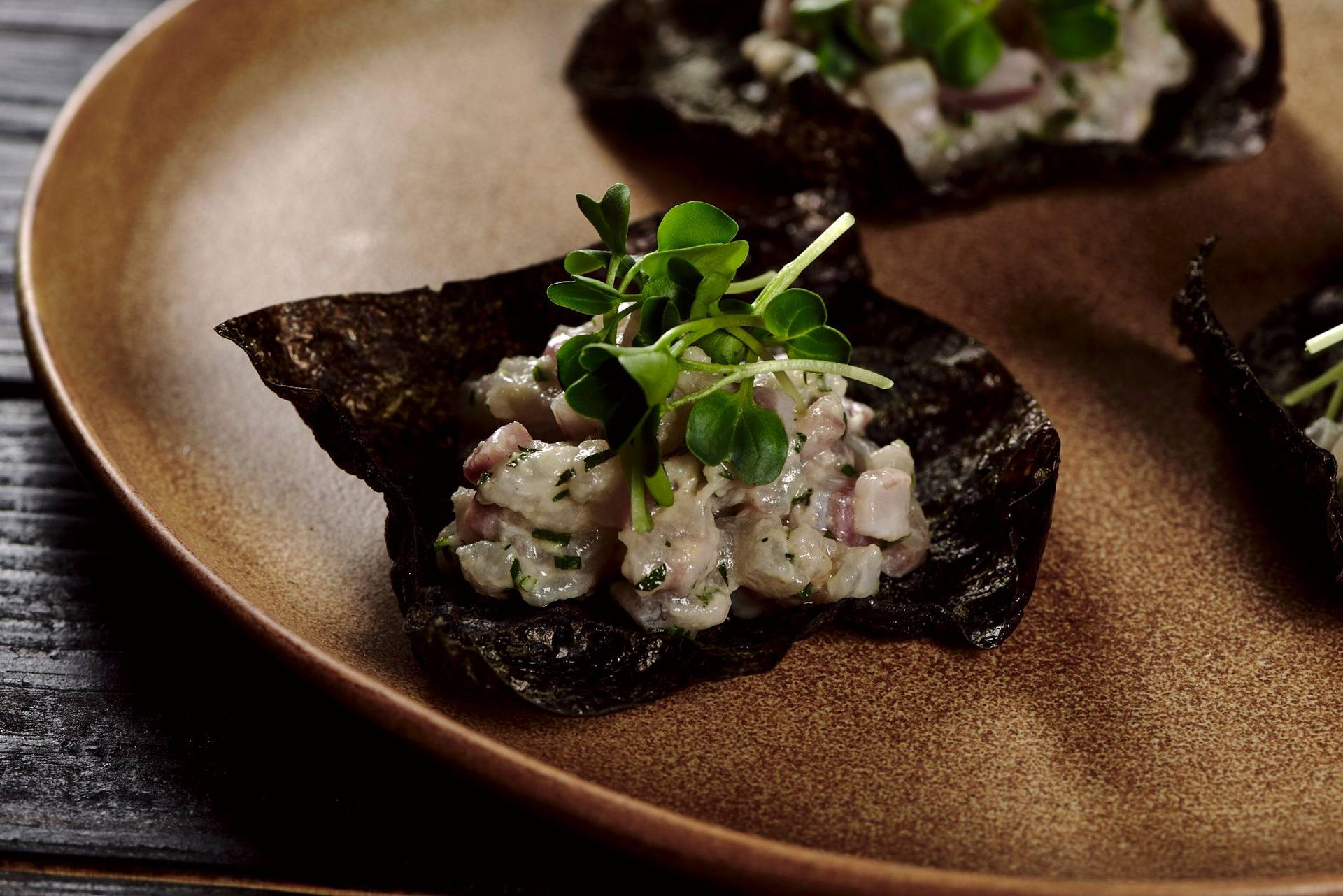 sea bass tartare with nori cracker on a brown ceramic plate with black wooden background